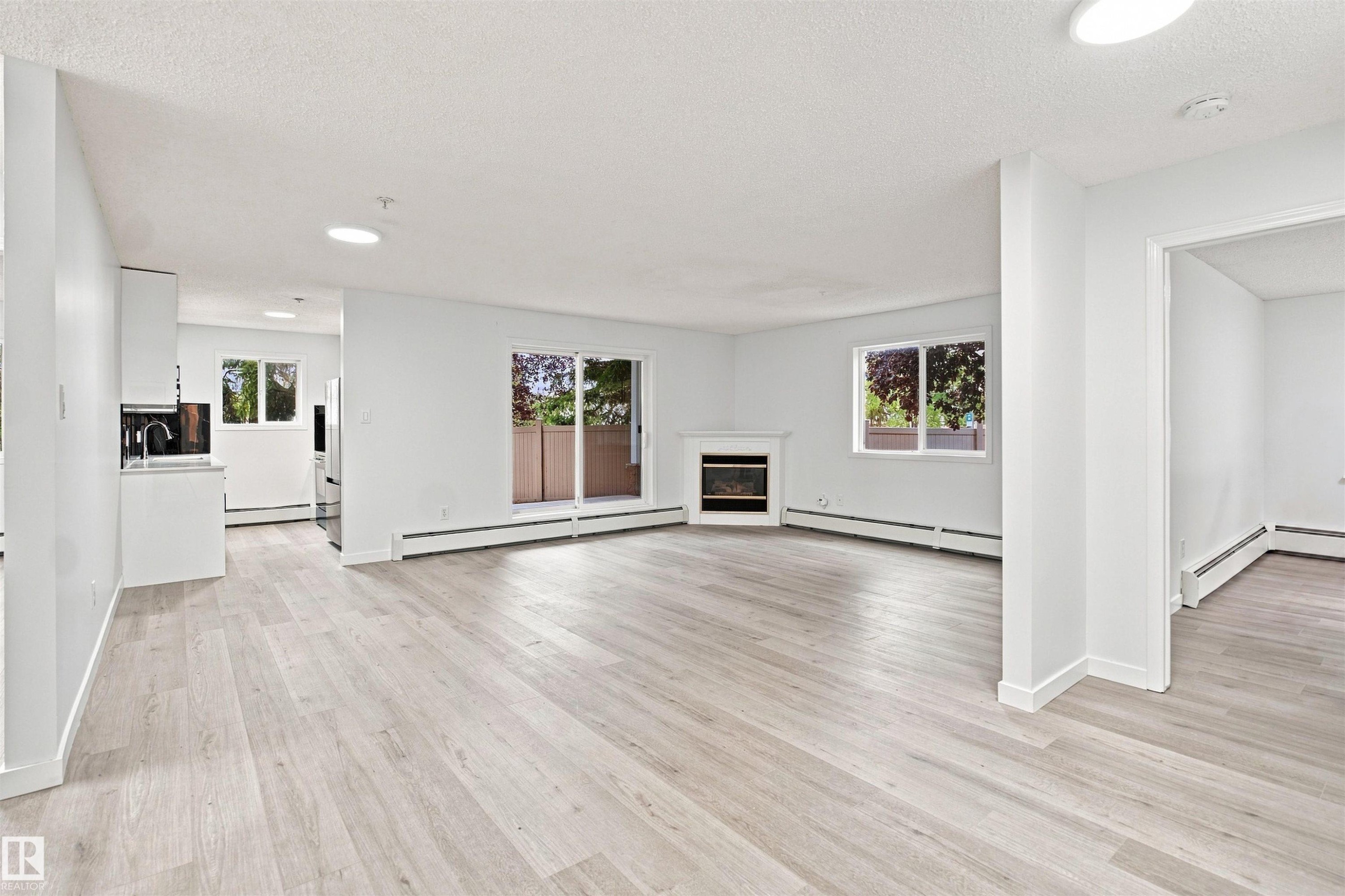 Light wood-finish flooring throughout, corner fireplace, sliding glass door with balcony, and ceiling-mounted light fixtures - #124 10511 42 Av Nw, Edmonton, AB