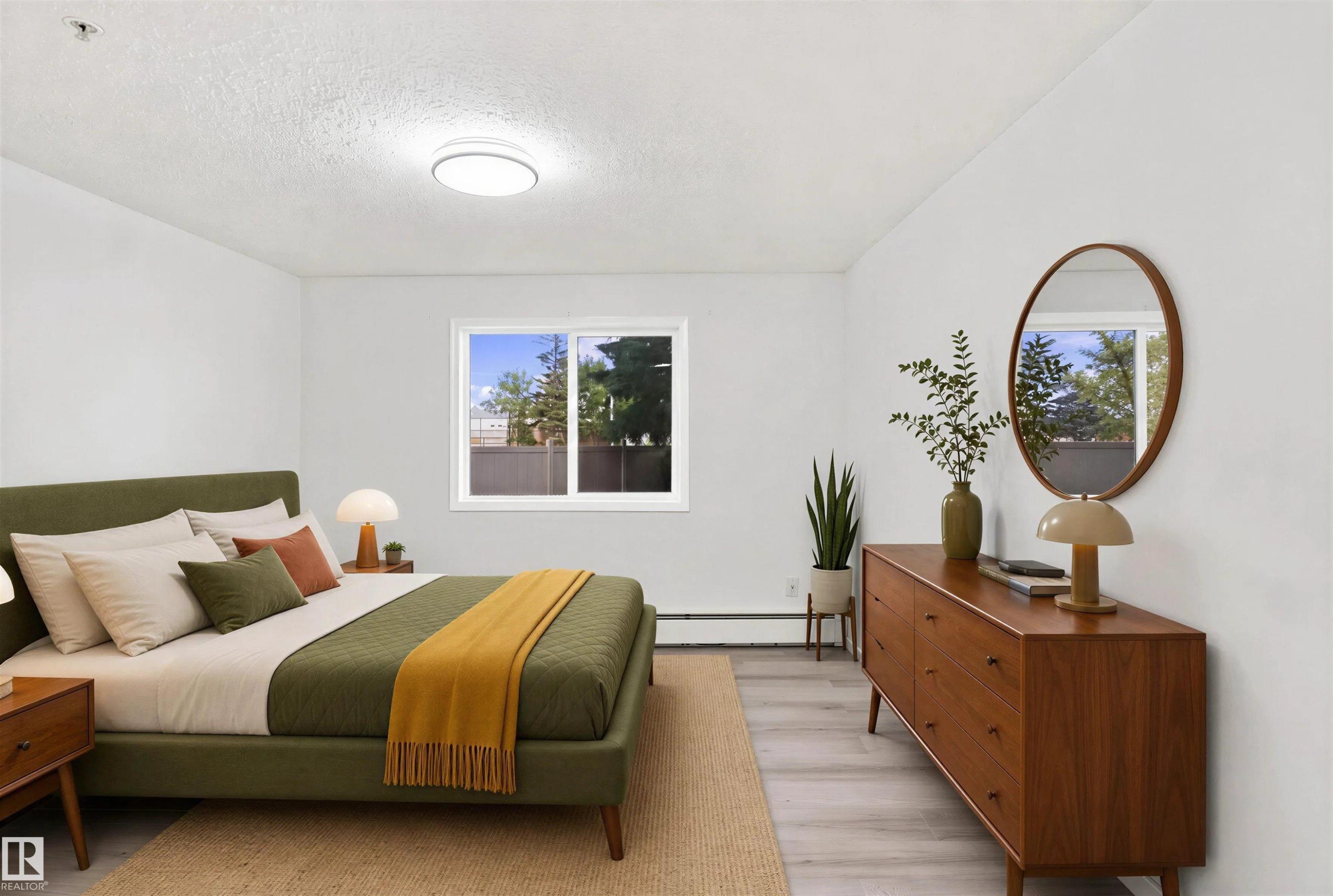 White walls, light wood-finish flooring, and a large window providing natural light - #124 10511 42 Av Nw, Edmonton, AB