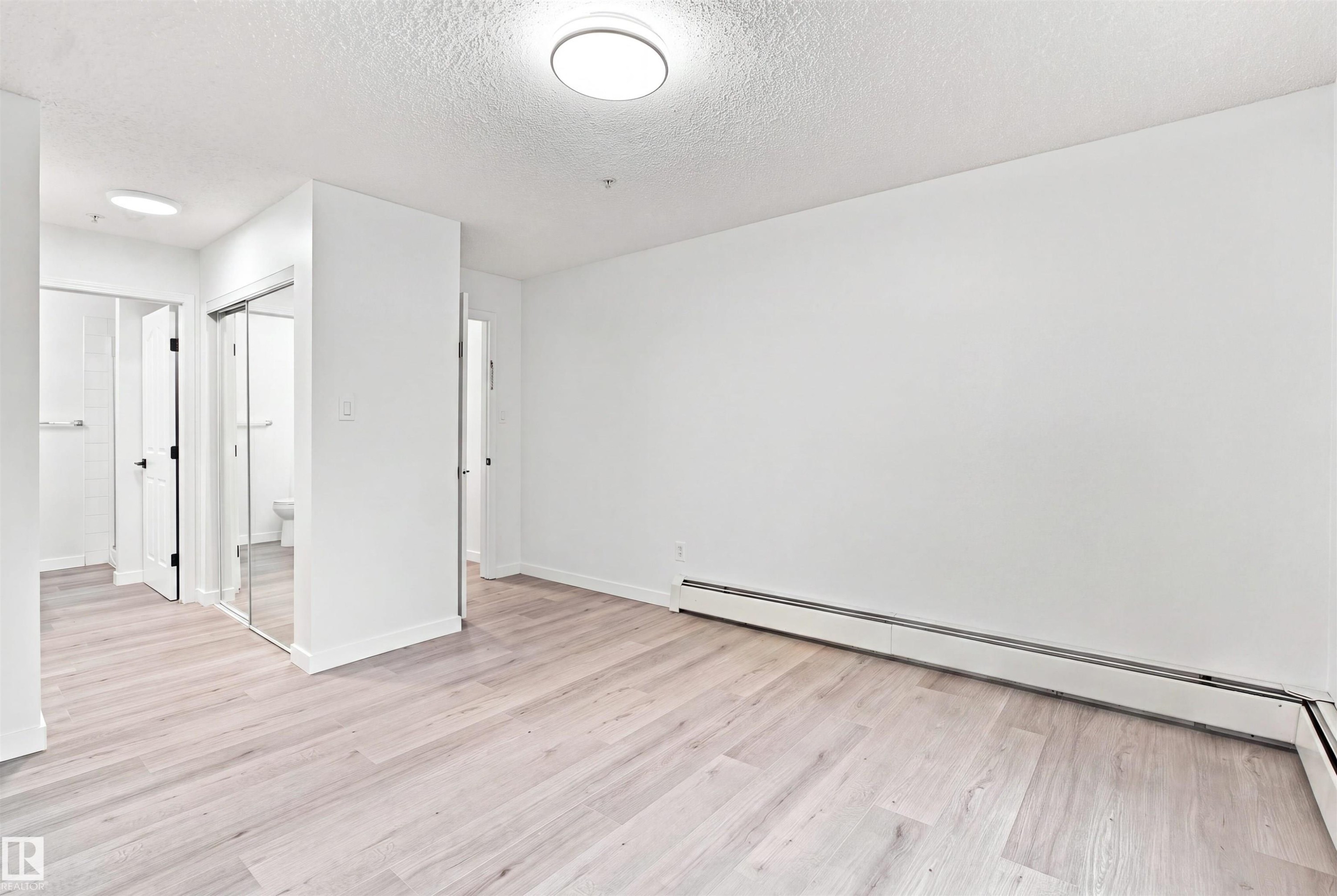 Wood-finish flooring, white walls, flush mount ceiling lighting, mirrored closet doors, and baseboard heating - #124 10511 42 Av Nw, Edmonton, AB