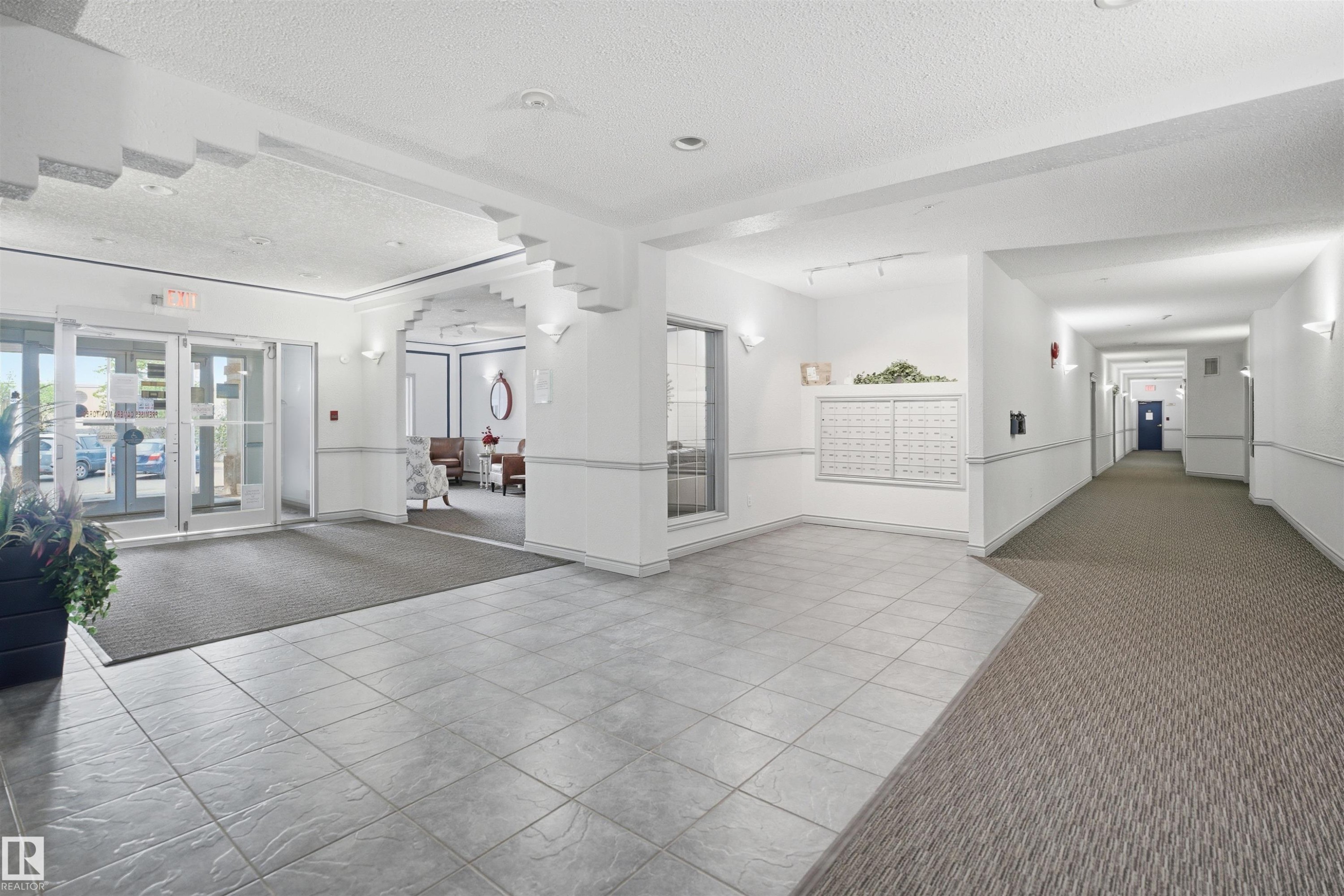 Lobby featuring tile flooring, glass entry doors, wall sconces, and a carpeted hallway - #124 10511 42 Av Nw, Edmonton, AB