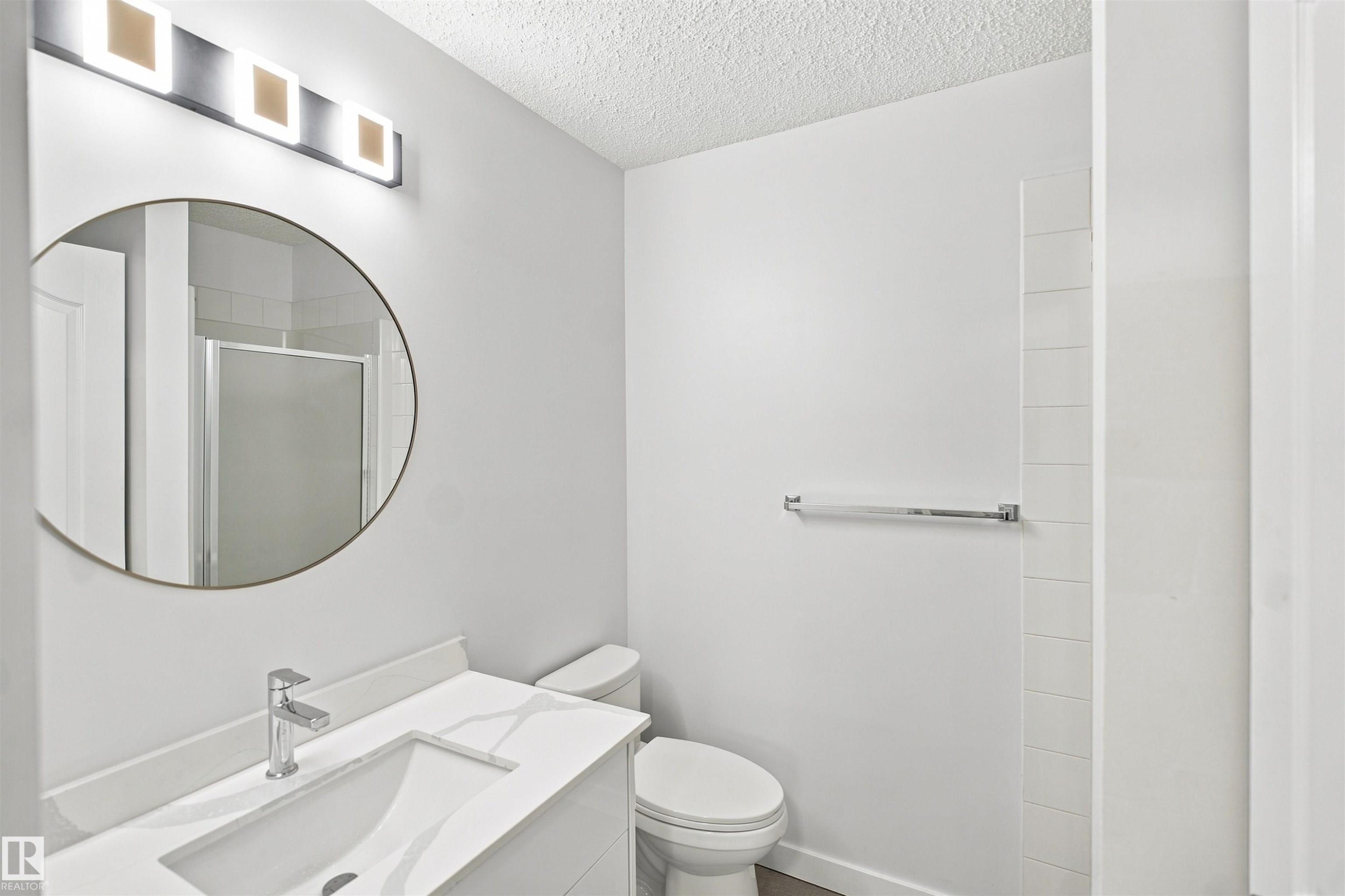 Modern vanity with an integrated sink, polished chrome faucet, round wall mirror, and a contemporary light fixture - #124 10511 42 Av Nw, Edmonton, AB
