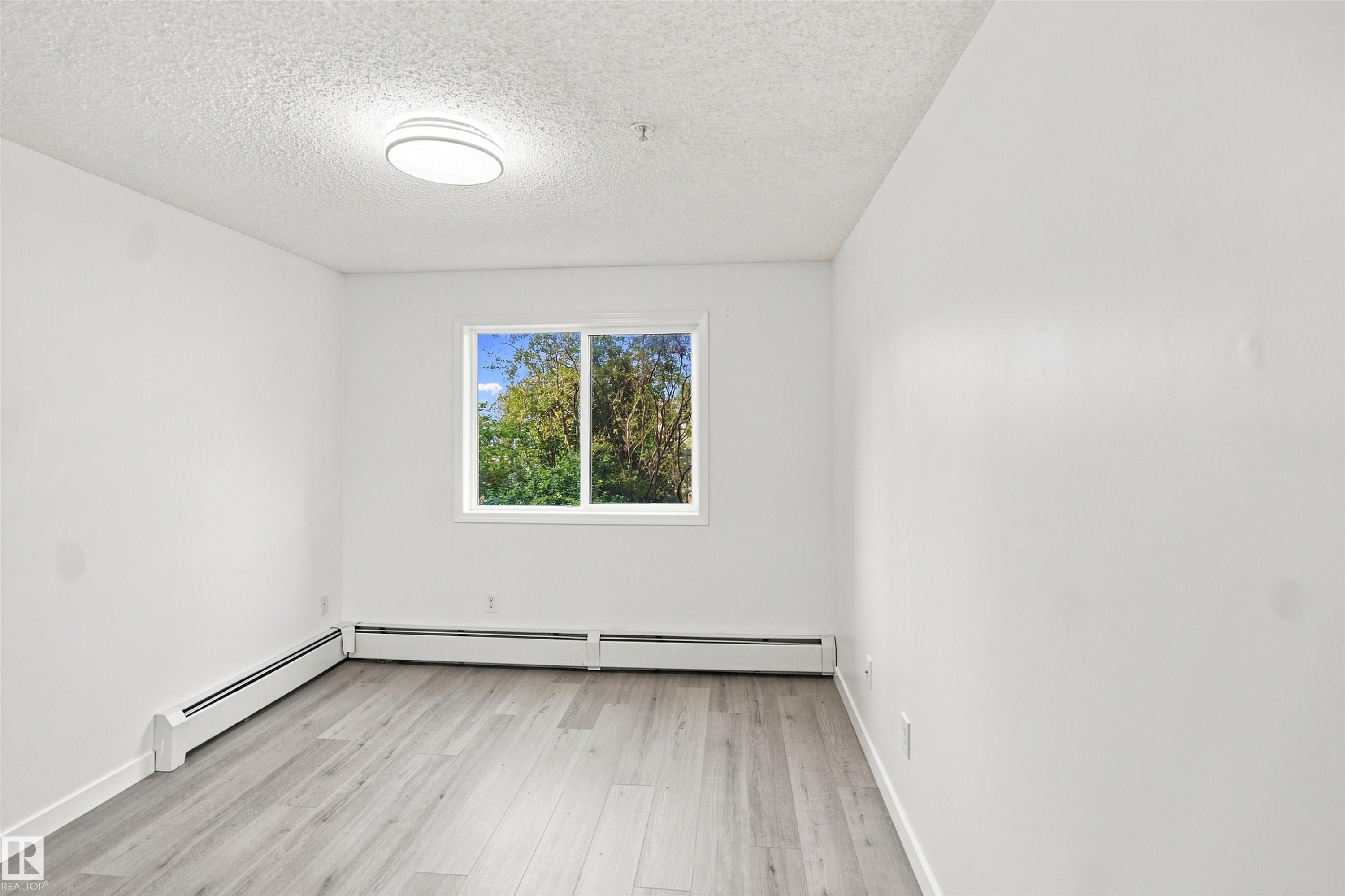 Light wood-finish flooring, white walls, and a large window providing natural light - #124 10511 42 Av Nw, Edmonton, AB