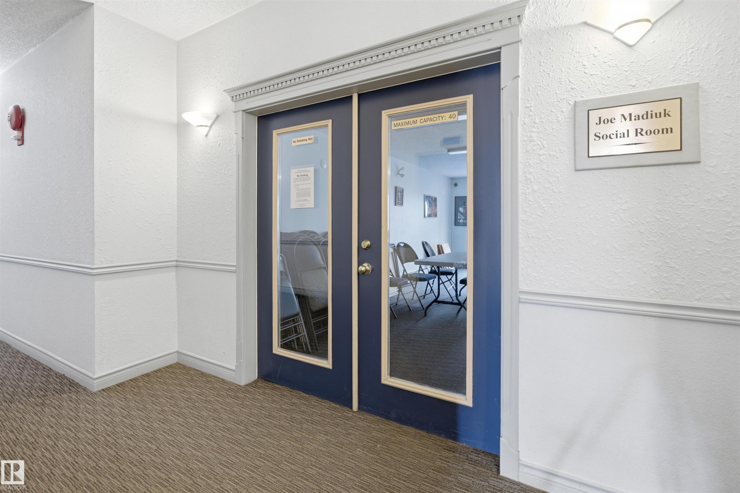 Double glass panel doors with decorative trim, wall-mounted sconces, and carpeted flooring - #124 10511 42 Av Nw, Edmonton, AB