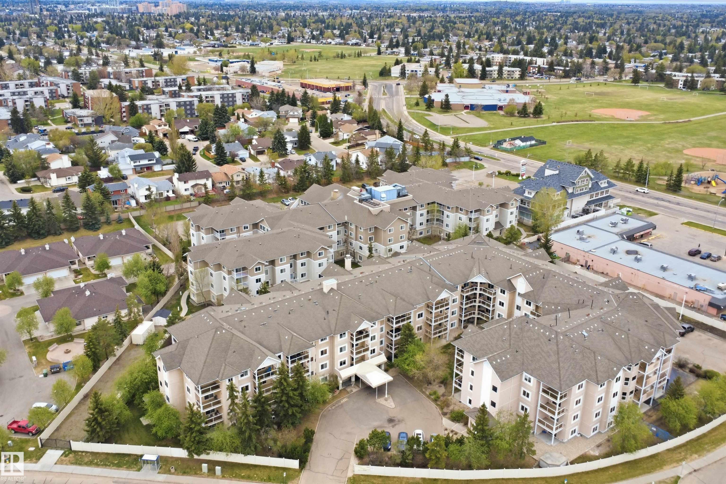 Multi-story residential complex featuring multiple balconies, a covered entrance, and extensive surrounding green spaces - #124 10511 42 Av Nw, Edmonton, AB