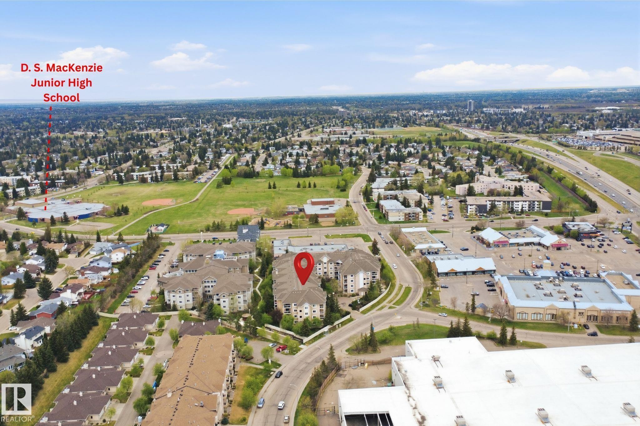 Aerial perspective showcasing a multi-story residential building, adjacent to a structured road network, with a large green space and educational facility in the distance - #124 10511 42 Av Nw, Edmonton, AB