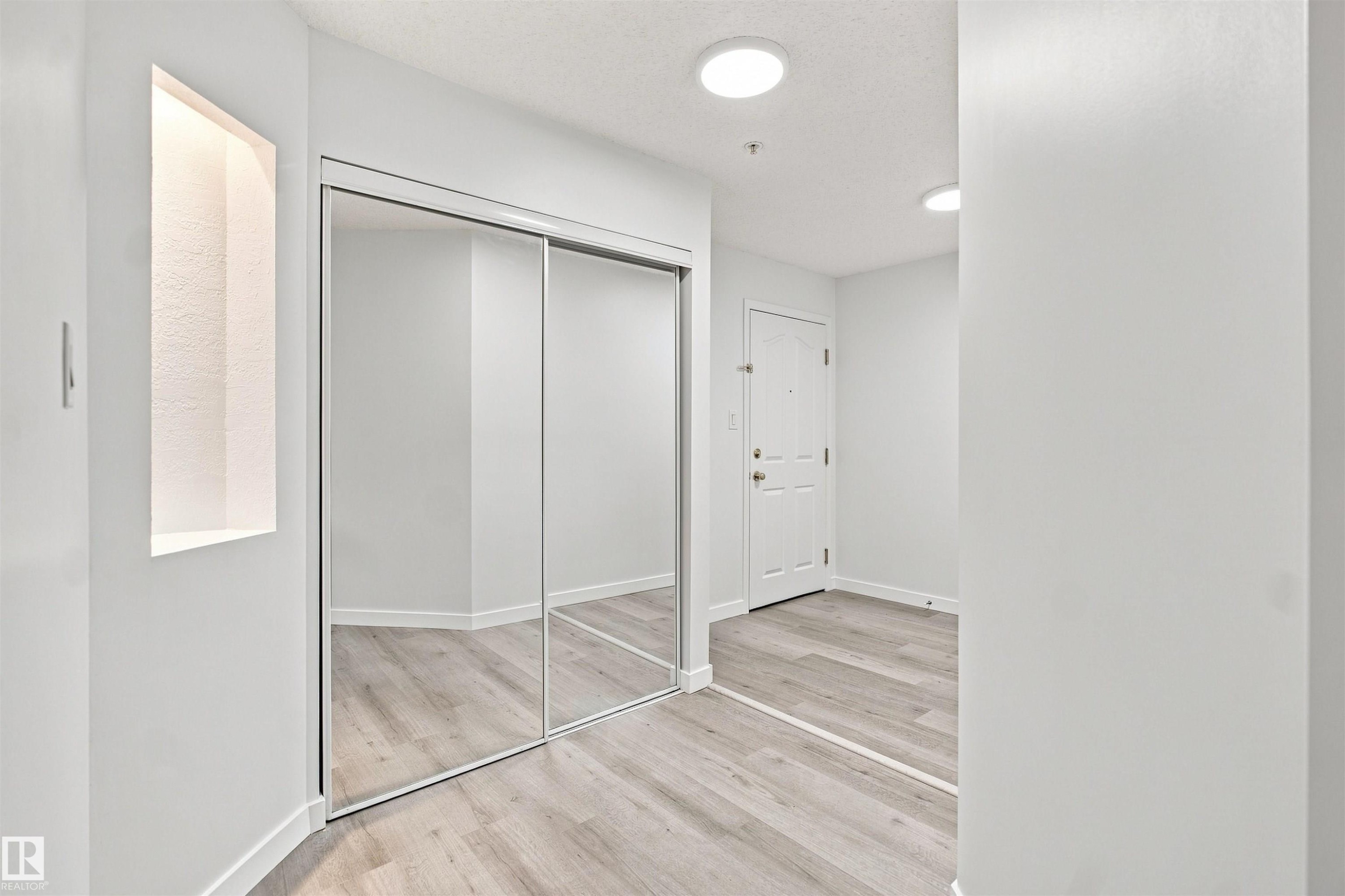 Mirrored sliding closet doors, wood-finish flooring, recessed wall niche with accent lighting, and flush-mount ceiling lighting - #124 10511 42 Av Nw, Edmonton, AB