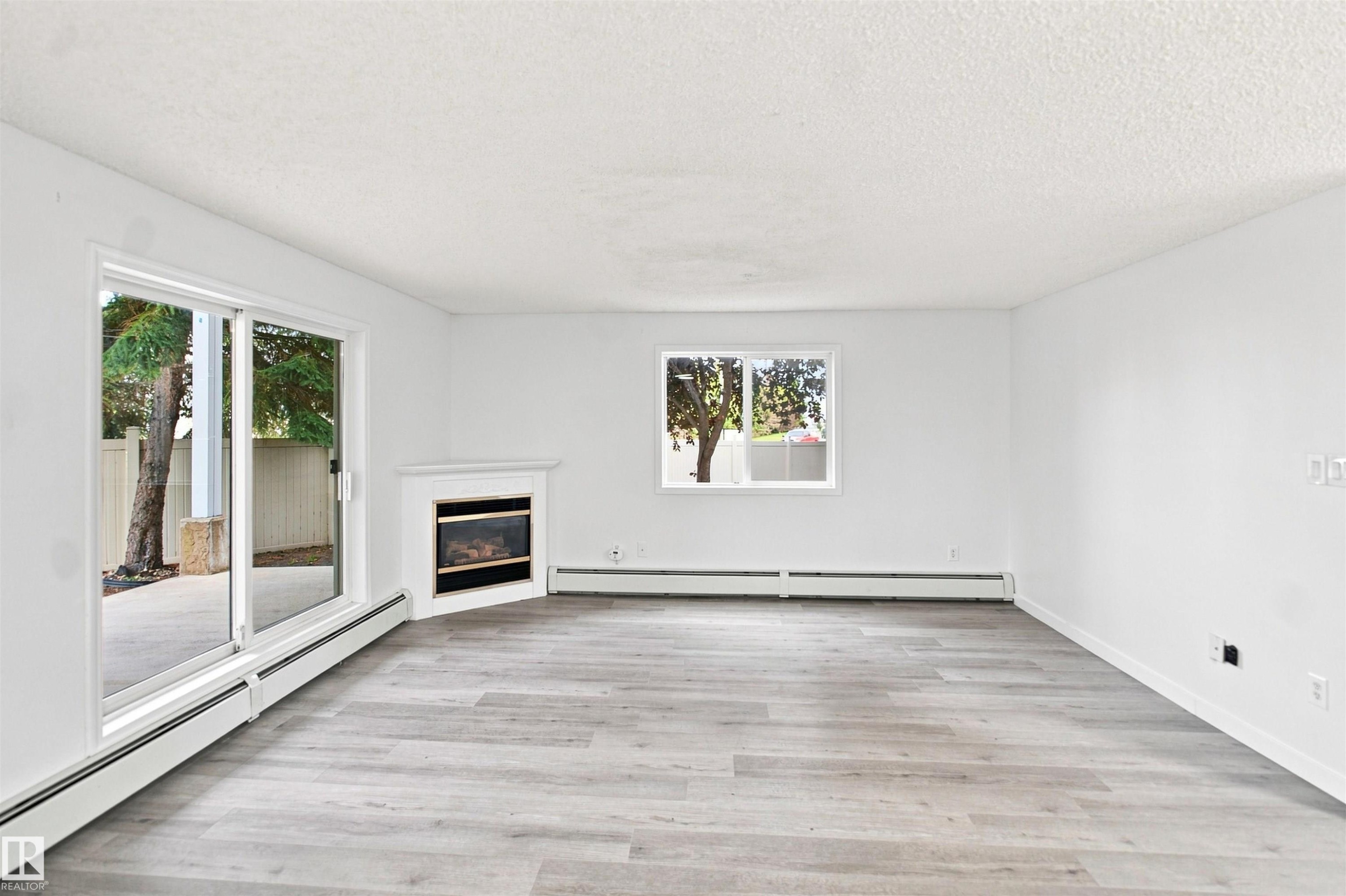 Light-toned wood-finish flooring, white walls, built-in fireplace, sliding glass door, and a single window - #124 10511 42 Av Nw, Edmonton, AB