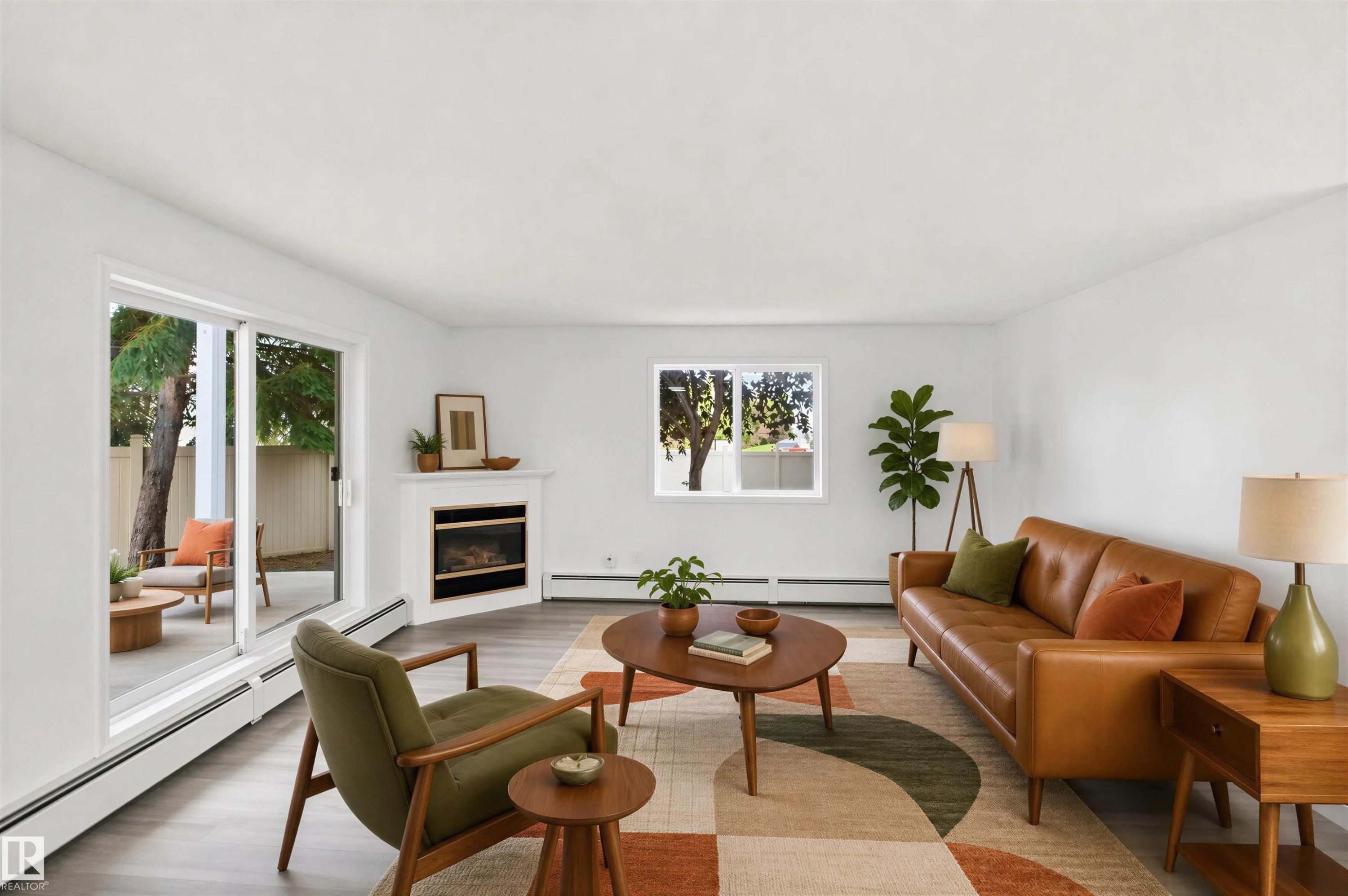 Spacious living area featuring wood-finish flooring, a corner fireplace with a white mantel, and a large sliding glass door - #124 10511 42 Av Nw, Edmonton, AB
