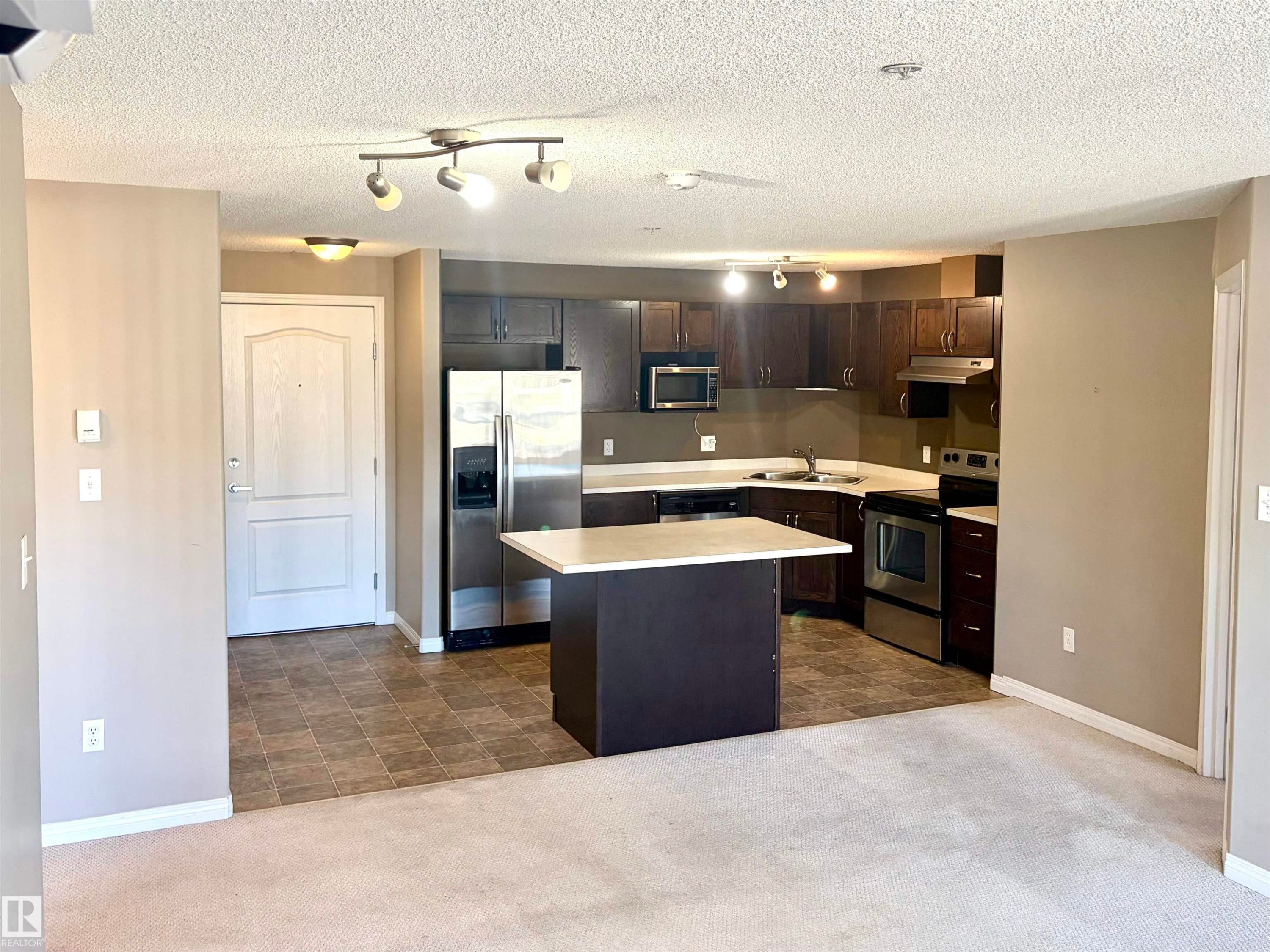 Kitchen featuring dark wood-finish cabinetry, stainless steel appliances, and a central island with a light-toned countertop - #1304 9363 Simpson Dr Nw, Edmonton, AB