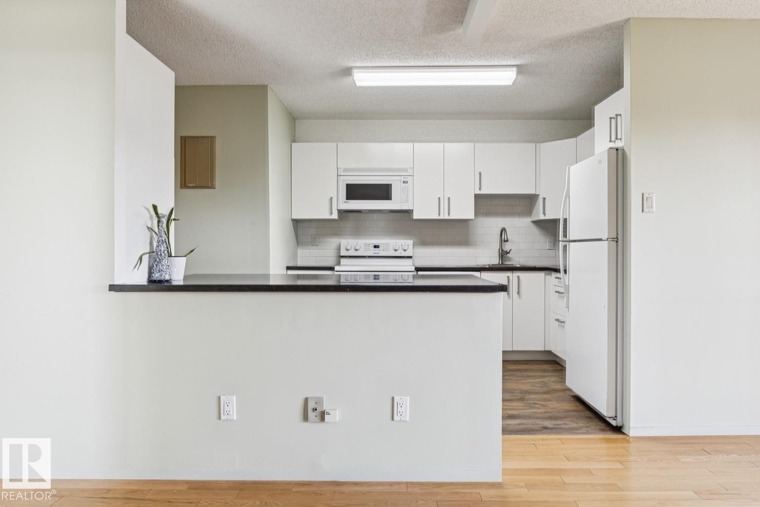 White cabinetry, stainless steel sink, black countertops, white subway tile backsplash, and wood-finish flooring - #905 9929 113 St Nw, Edmonton, AB