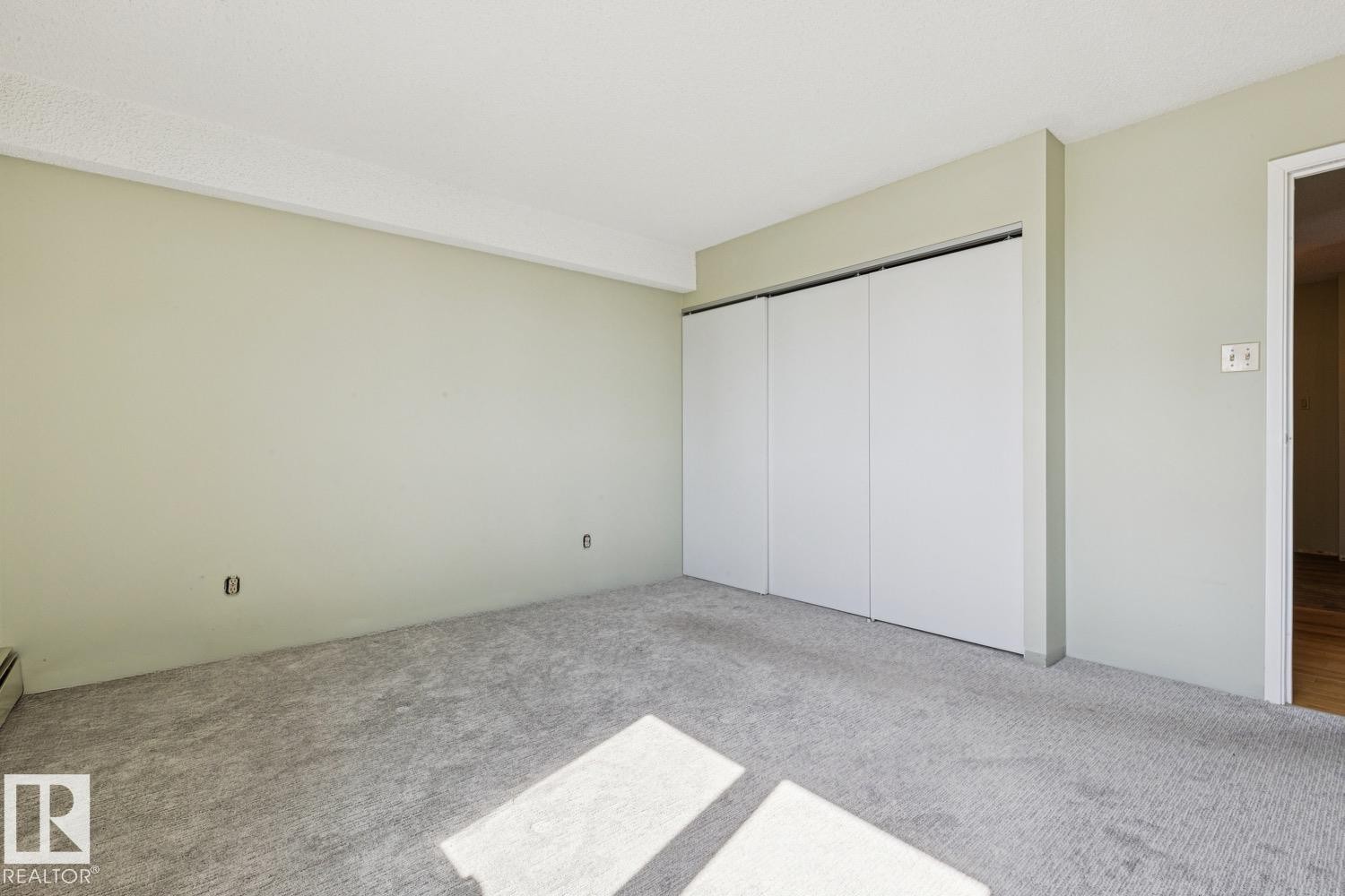 Carpeted room featuring a white ceiling, light-toned walls, and a multi-panel closet with white doors - #905 9929 113 St Nw, Edmonton, AB