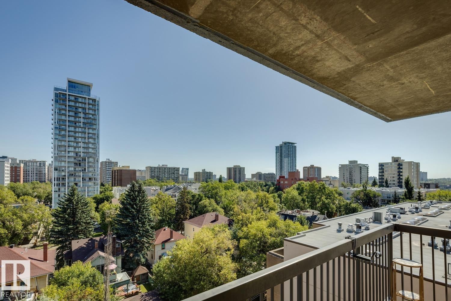 Balcony with black metal railing overlooking a cityscape with mature trees and diverse architectural styles - #905 9929 113 St Nw, Edmonton, AB
