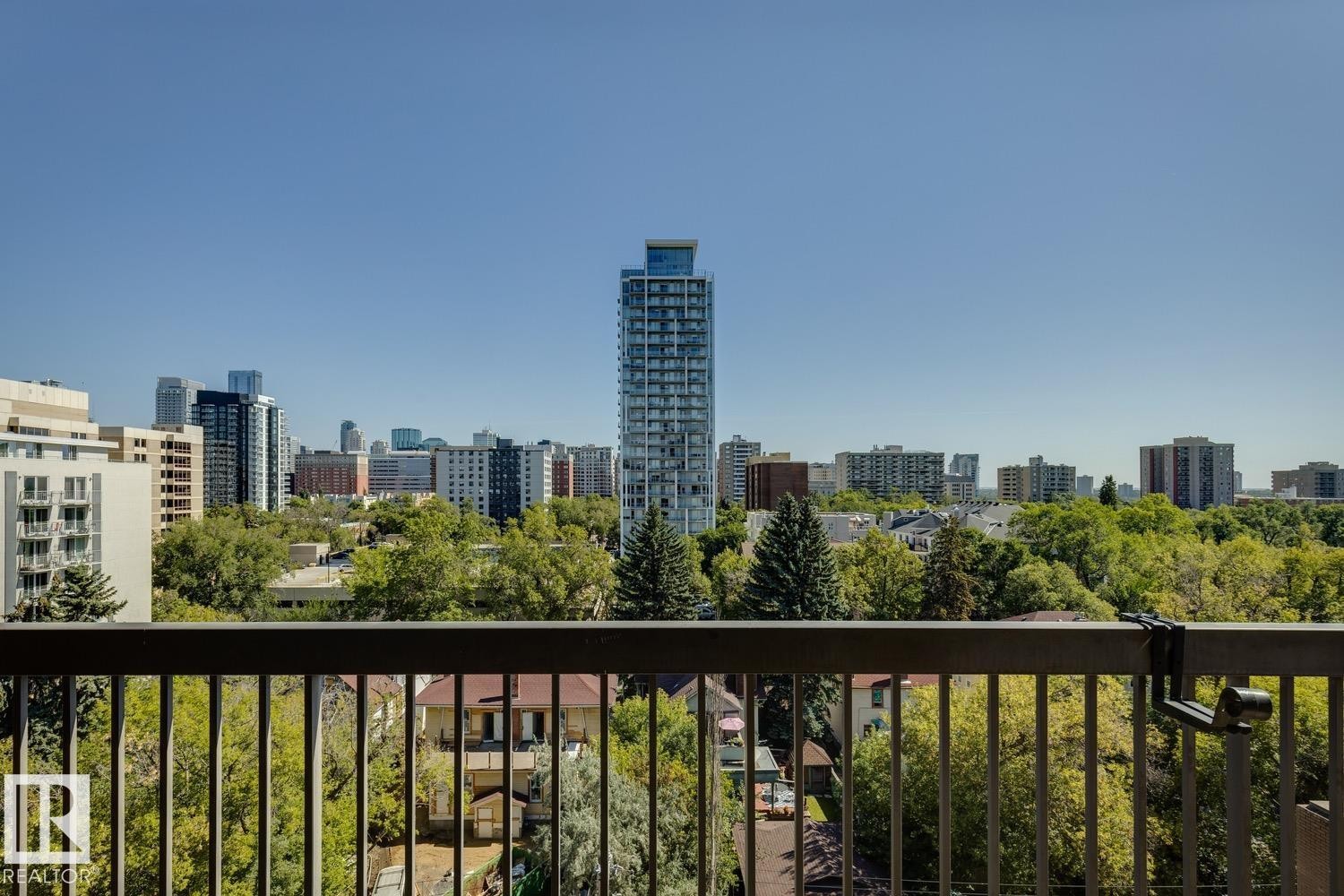Urban skyline backdrop with a variety of architectural styles, expansive green tree canopy, and a black metal railing - #905 9929 113 St Nw, Edmonton, AB
