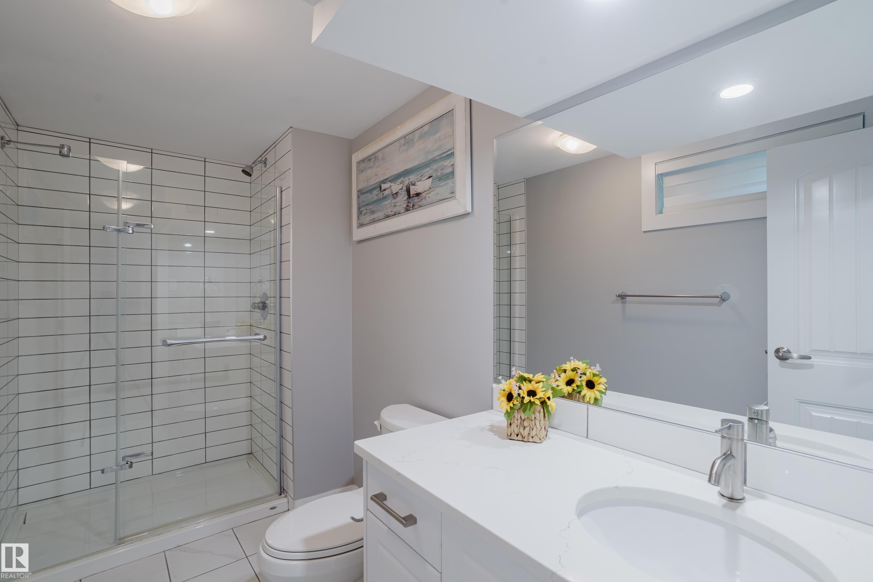 Glass-enclosed shower with subway tile surround, single vanity with integrated sink, polished chrome faucet, and expansive wall-mounted mirror - 4708 106 Avenue Nw, Edmonton, AB