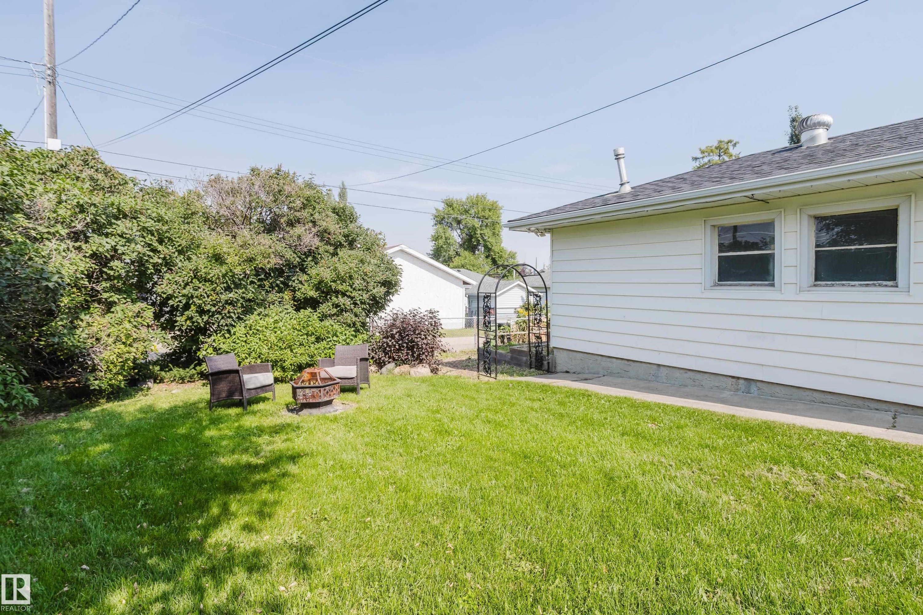 Expansive green lawn with mature perimeter shrubbery and a white siding exterior - 4708 106 Avenue Nw, Edmonton, AB