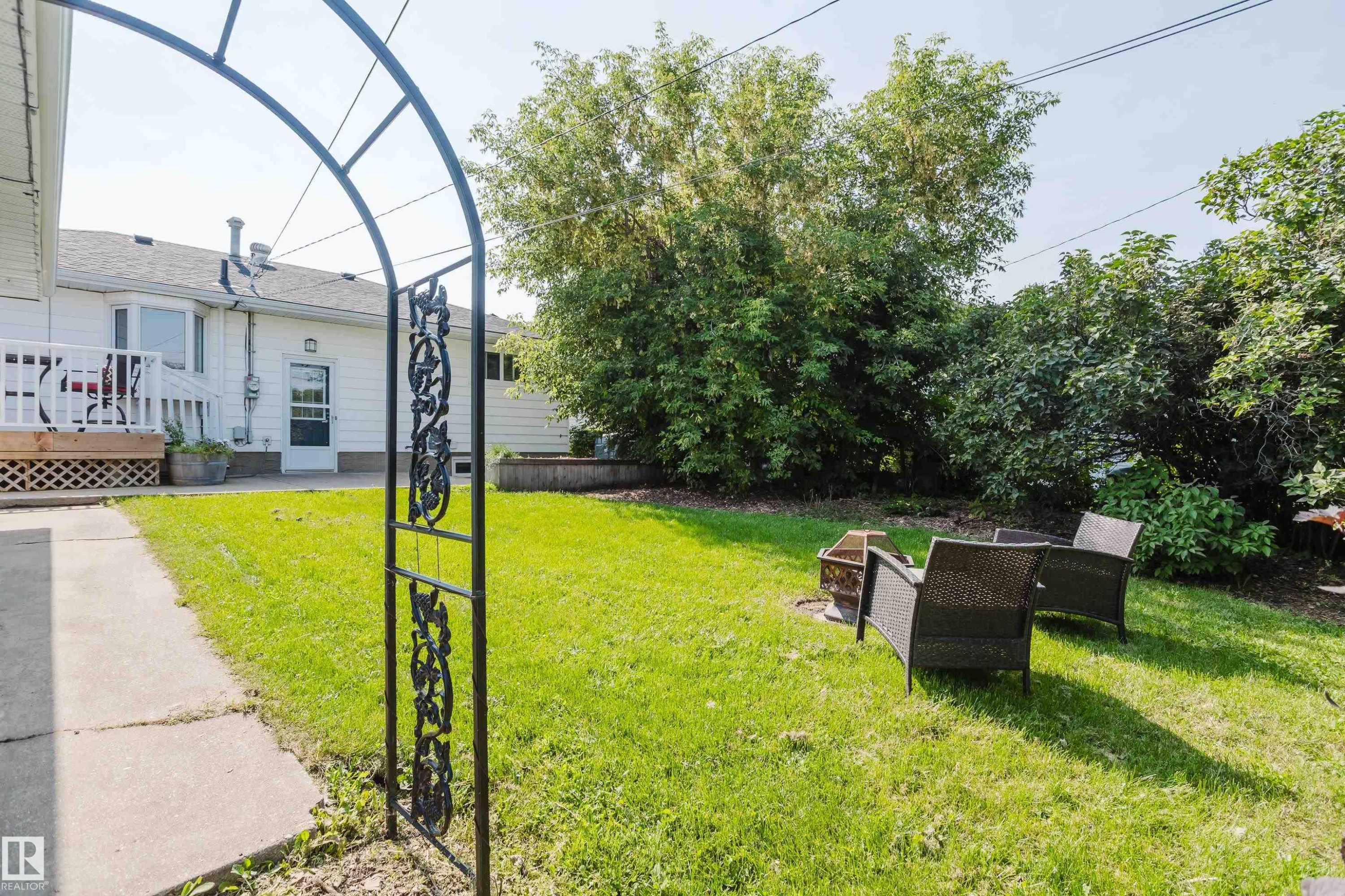 Expansive green lawn, mature perimeter trees, concrete walkway, decorative metal archway, and raised garden bed - 4708 106 Avenue Nw, Edmonton, AB