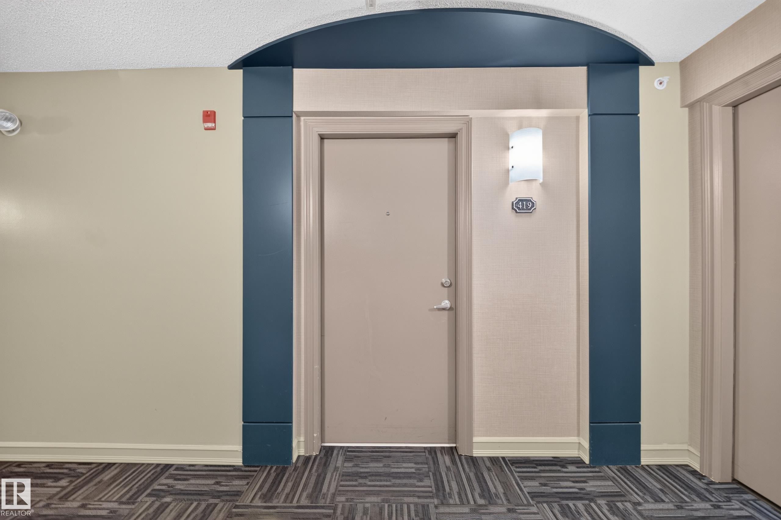 Entryway featuring a decorative arched doorway, wall sconce, and patterned carpet flooring - #419 4407 23 St Nw, Edmonton, AB