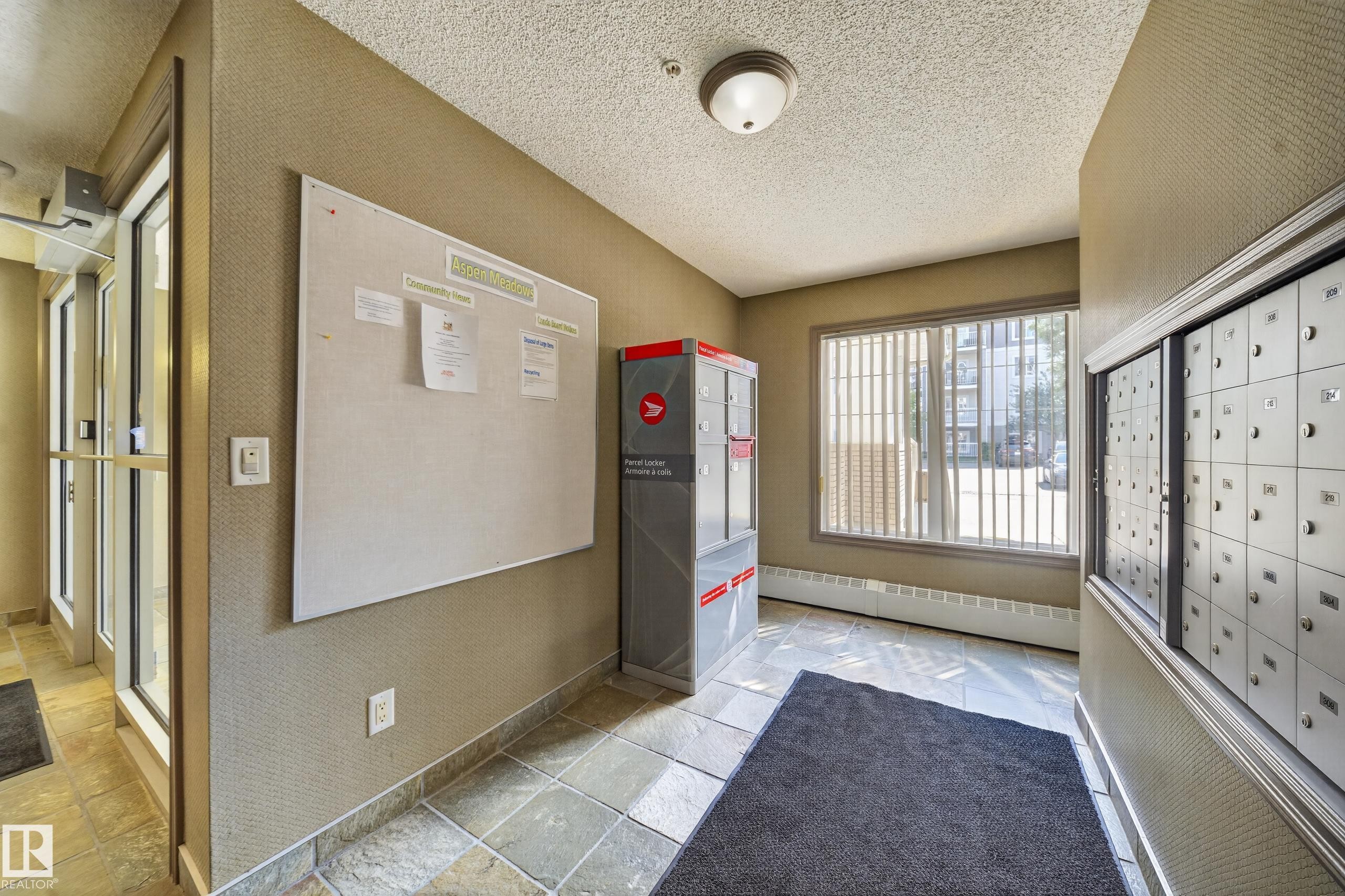 Tiled flooring, large window with blinds, wall-mounted mailboxes, and an interior bulletin board - #419 4407 23 St Nw, Edmonton, AB
