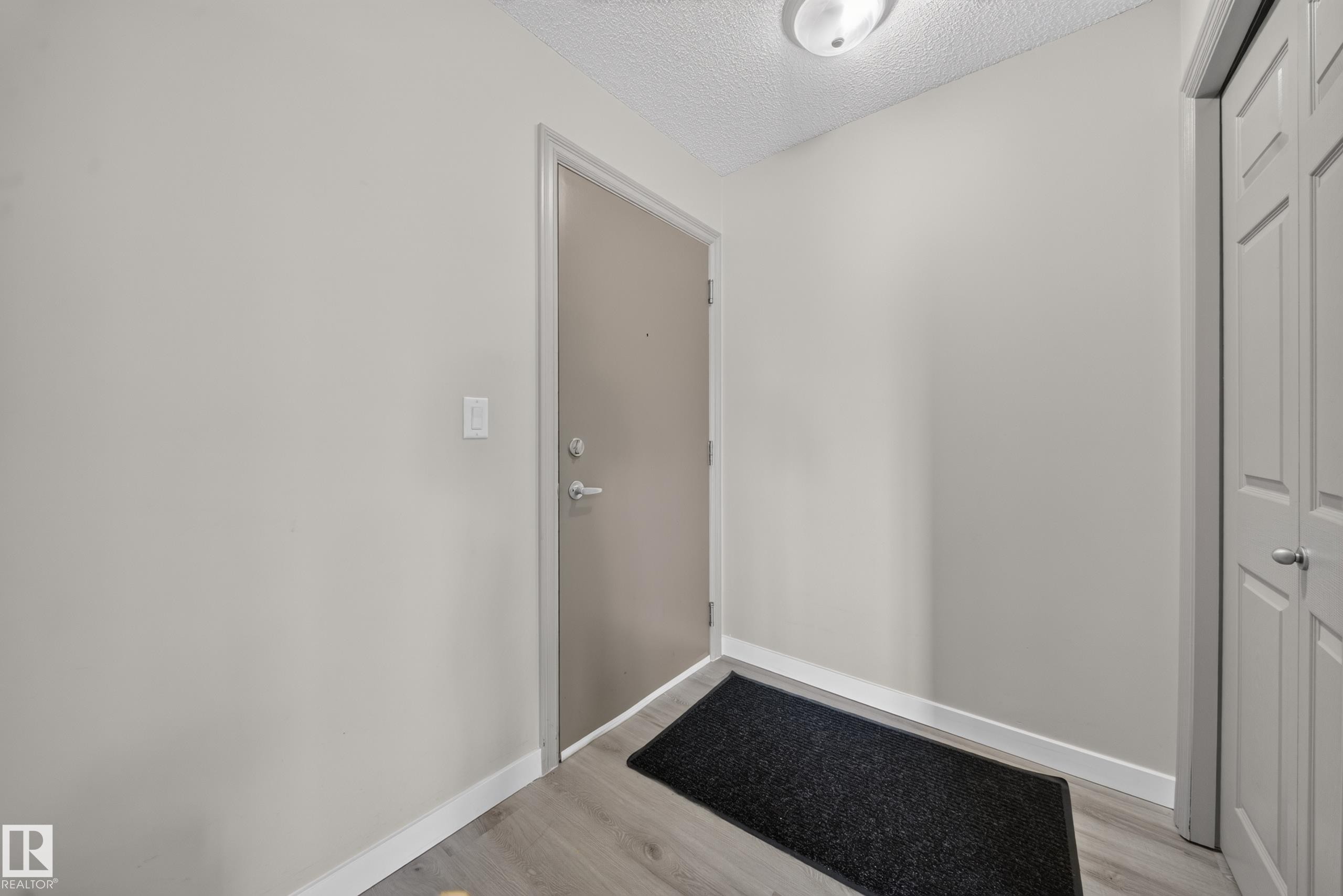 Entryway featuring a solid core door, wood-finish flooring, and bi-fold closet doors - #419 4407 23 St Nw, Edmonton, AB