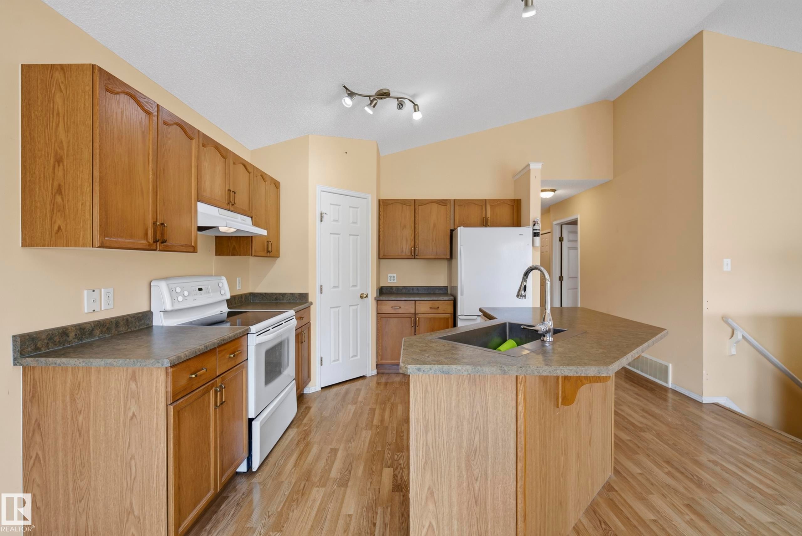 Kitchen featuring wood-finish cabinetry, solid surface countertops, a white appliance package, and a kitchen island with an undermount sink - 15213 49A Street Nw, Edmonton, AB