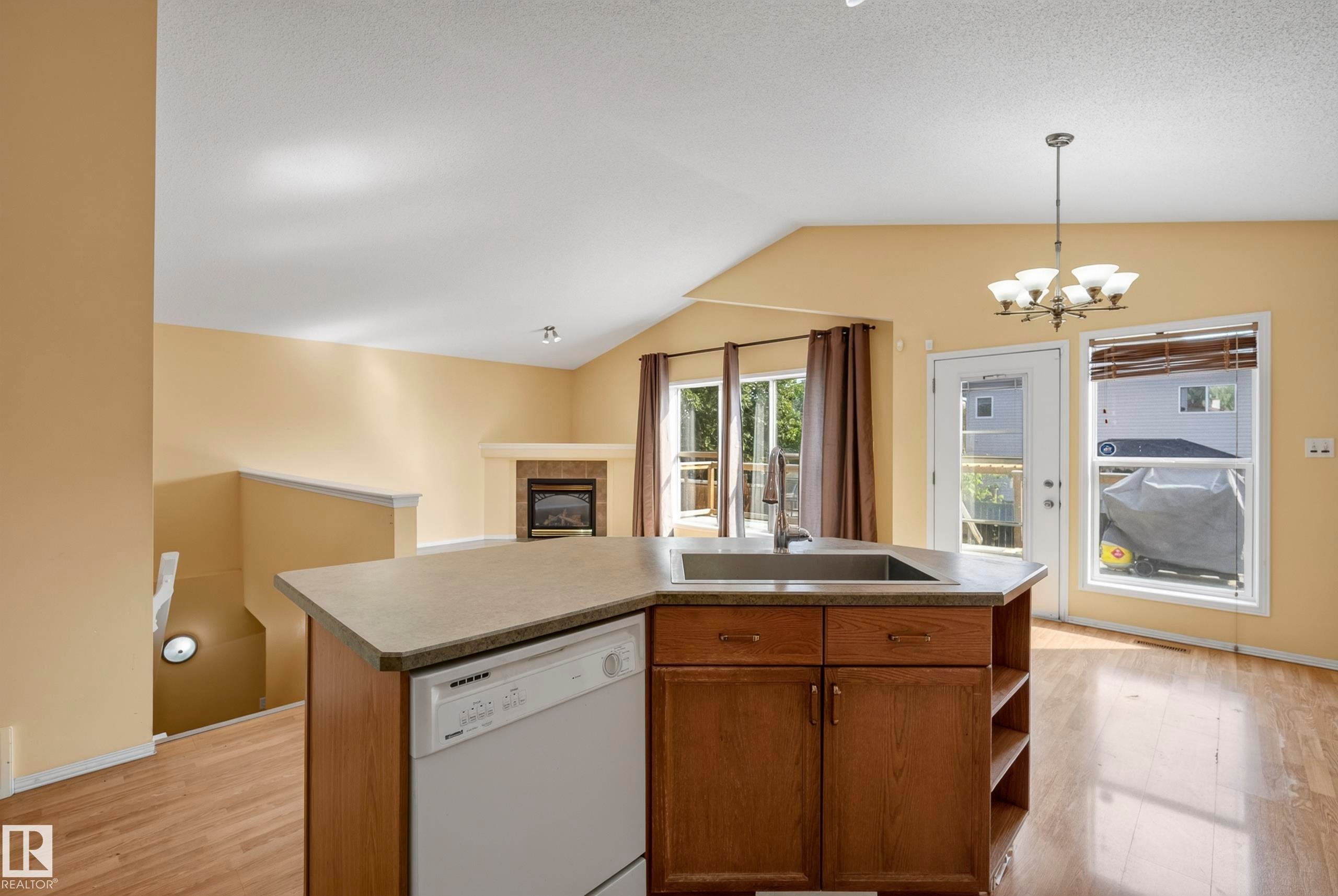 Kitchen island with integrated sink, wood-finish flooring, vaulted ceiling, corner fireplace, and rear deck access - 15213 49A Street Nw, Edmonton, AB