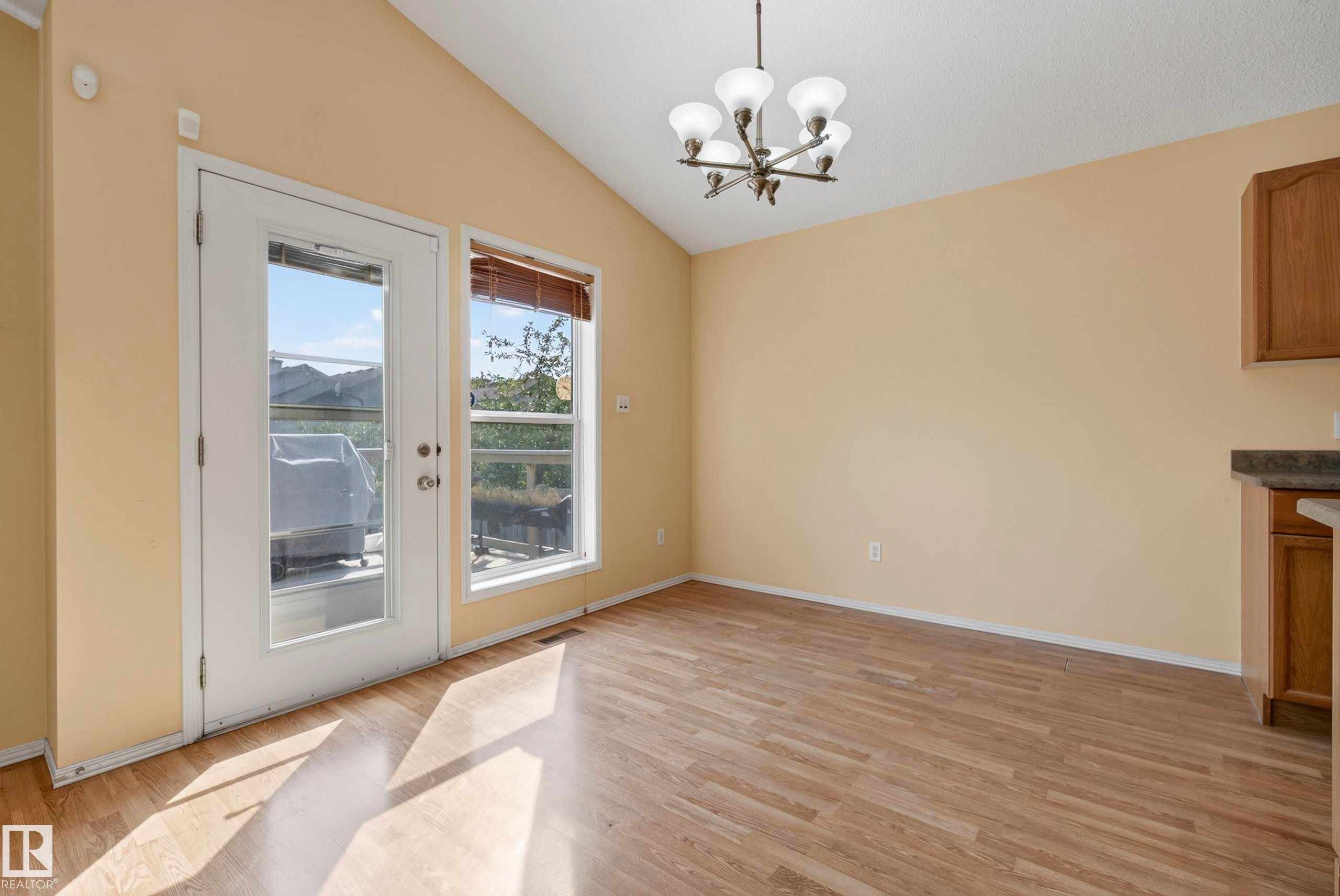 Vaulted ceiling with a multi-light chandelier, wood-finish flooring, and a glass-paneled door - 15213 49A Street Nw, Edmonton, AB