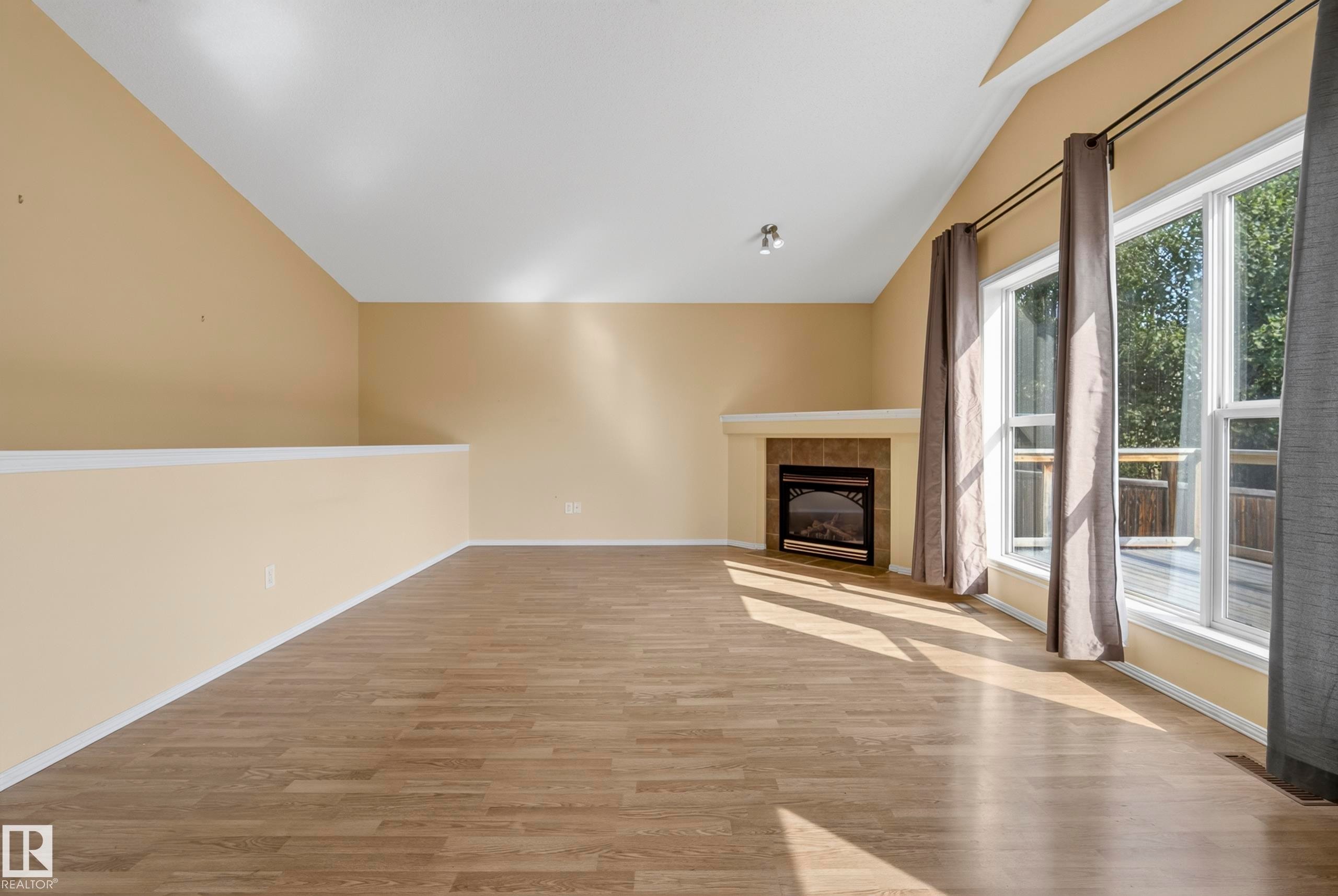 Vaulted ceiling with track lighting, wood-finish flooring, and a fireplace featuring a tile surround and mantel - 15213 49A Street Nw, Edmonton, AB