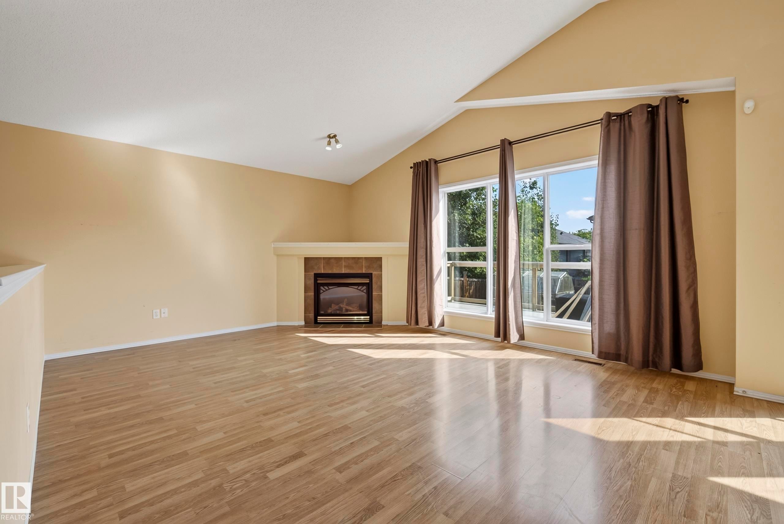 Vaulted ceiling, wood-finish flooring, large windows, tiled fireplace with mantel, and track lighting - 15213 49A Street Nw, Edmonton, AB