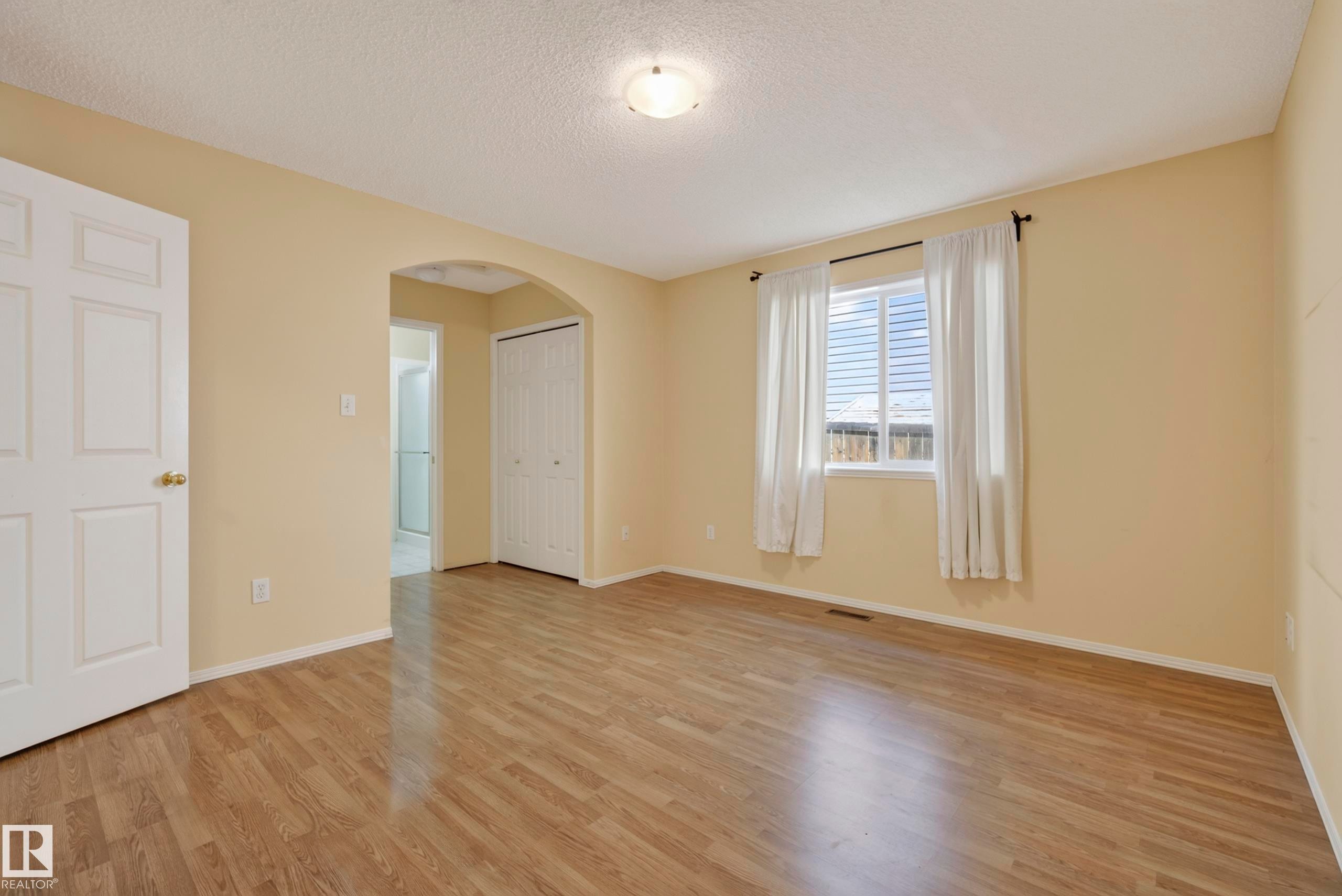 Wood-finish flooring, neutral wall tones, arched doorway, bi-fold closet doors, and recessed window - 15213 49A Street Nw, Edmonton, AB