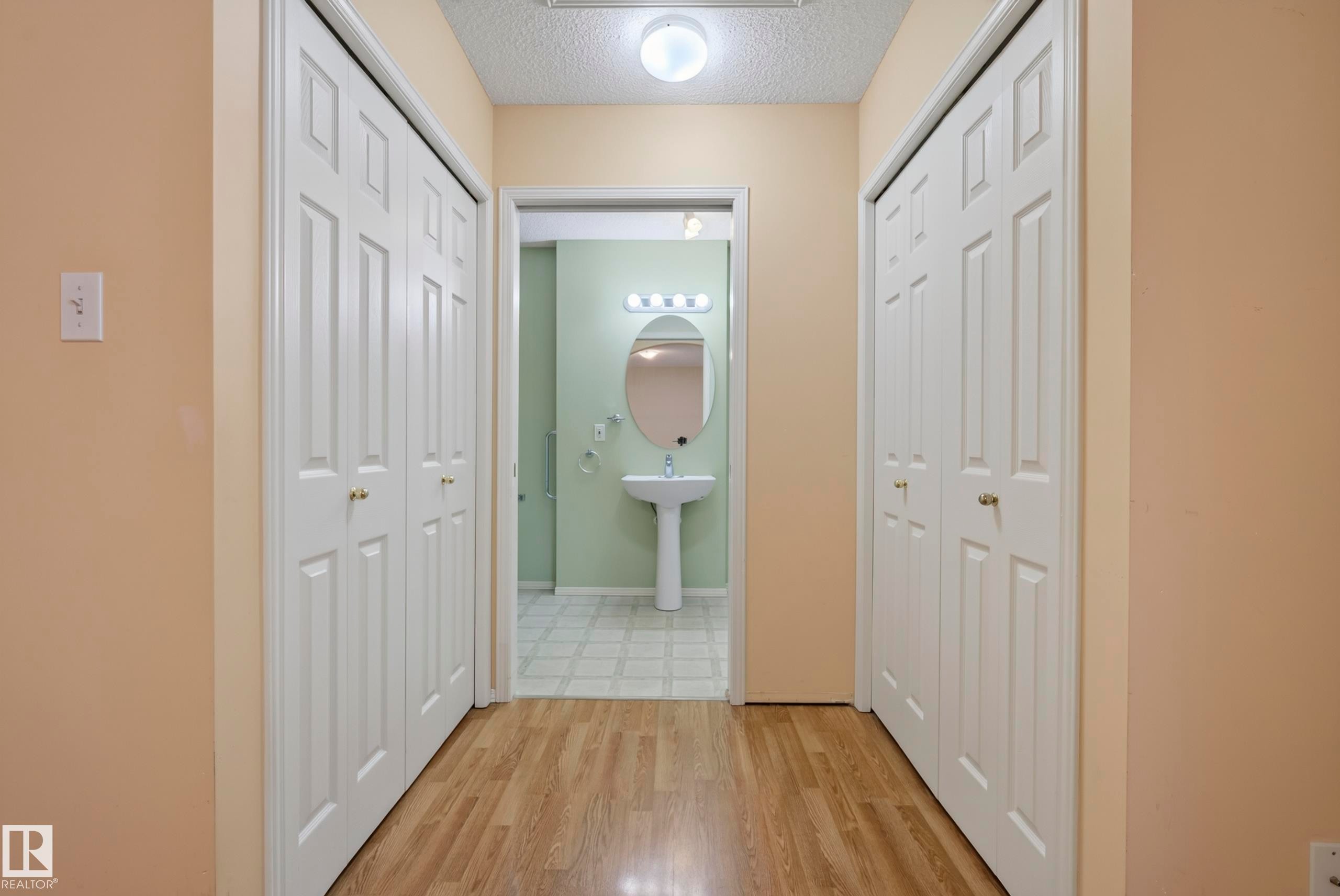 Hallway featuring wood-finish flooring and bi-fold panel doors - 15213 49A Street Nw, Edmonton, AB