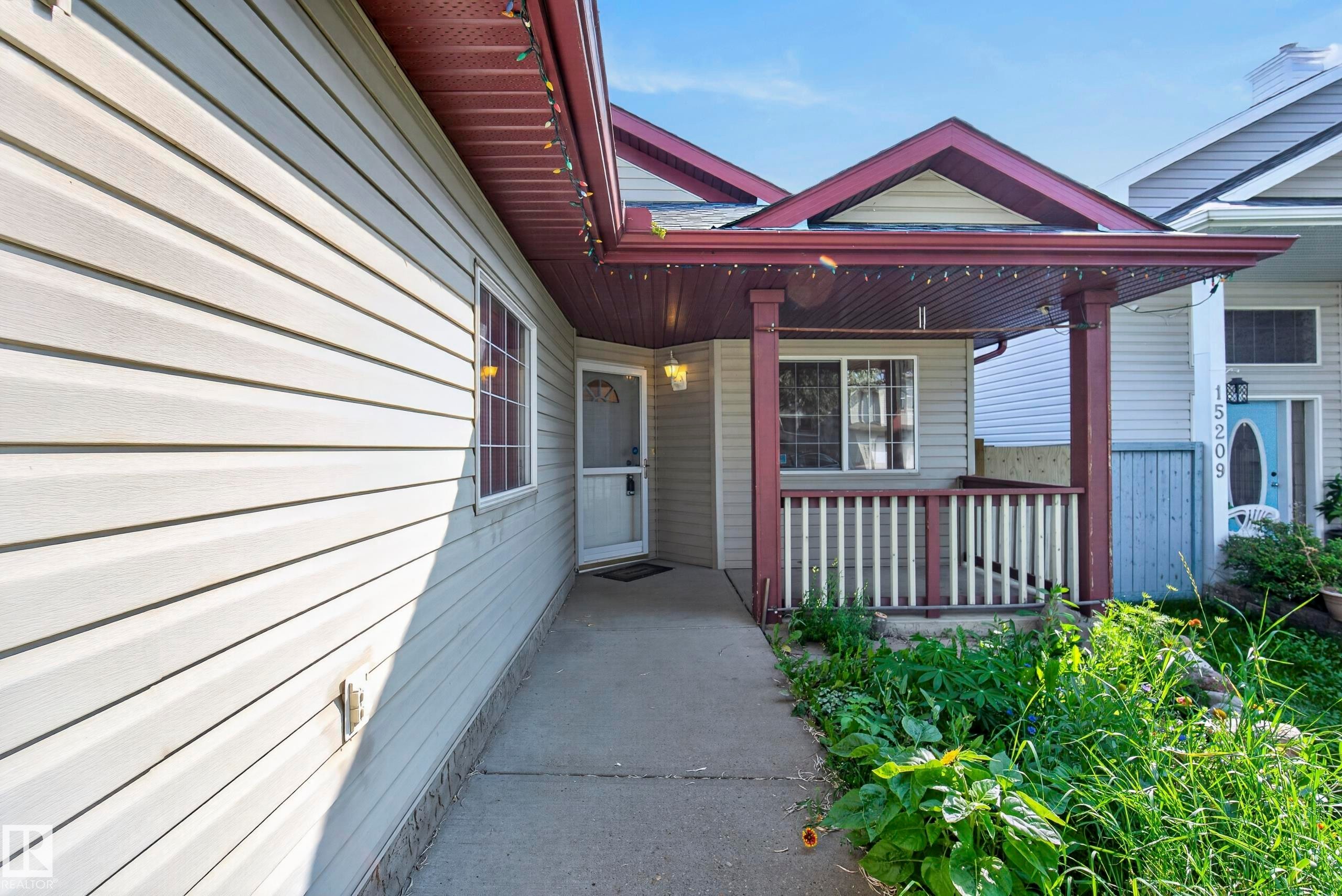 Light-colored horizontal siding exterior with a covered porch featuring a white railing and dark trim - 15213 49A Street Nw, Edmonton, AB