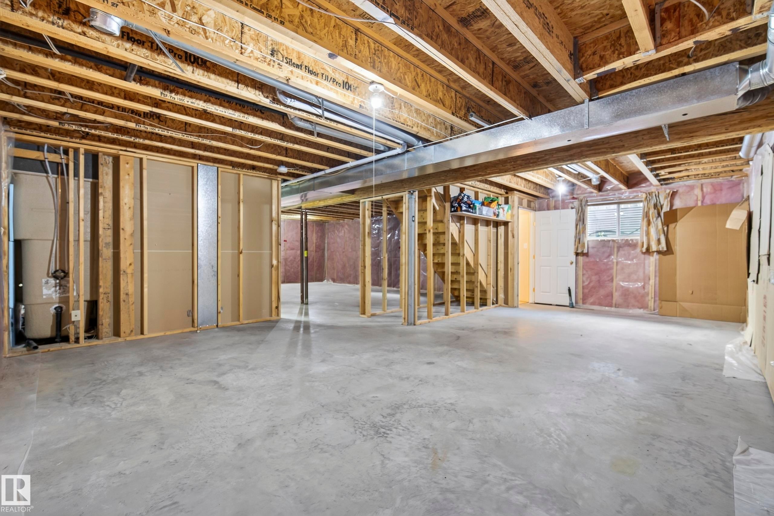 Unfinished lower level with exposed wood framing, concrete flooring, exposed ceiling joists, and a partial staircase - 15213 49A Street Nw, Edmonton, AB