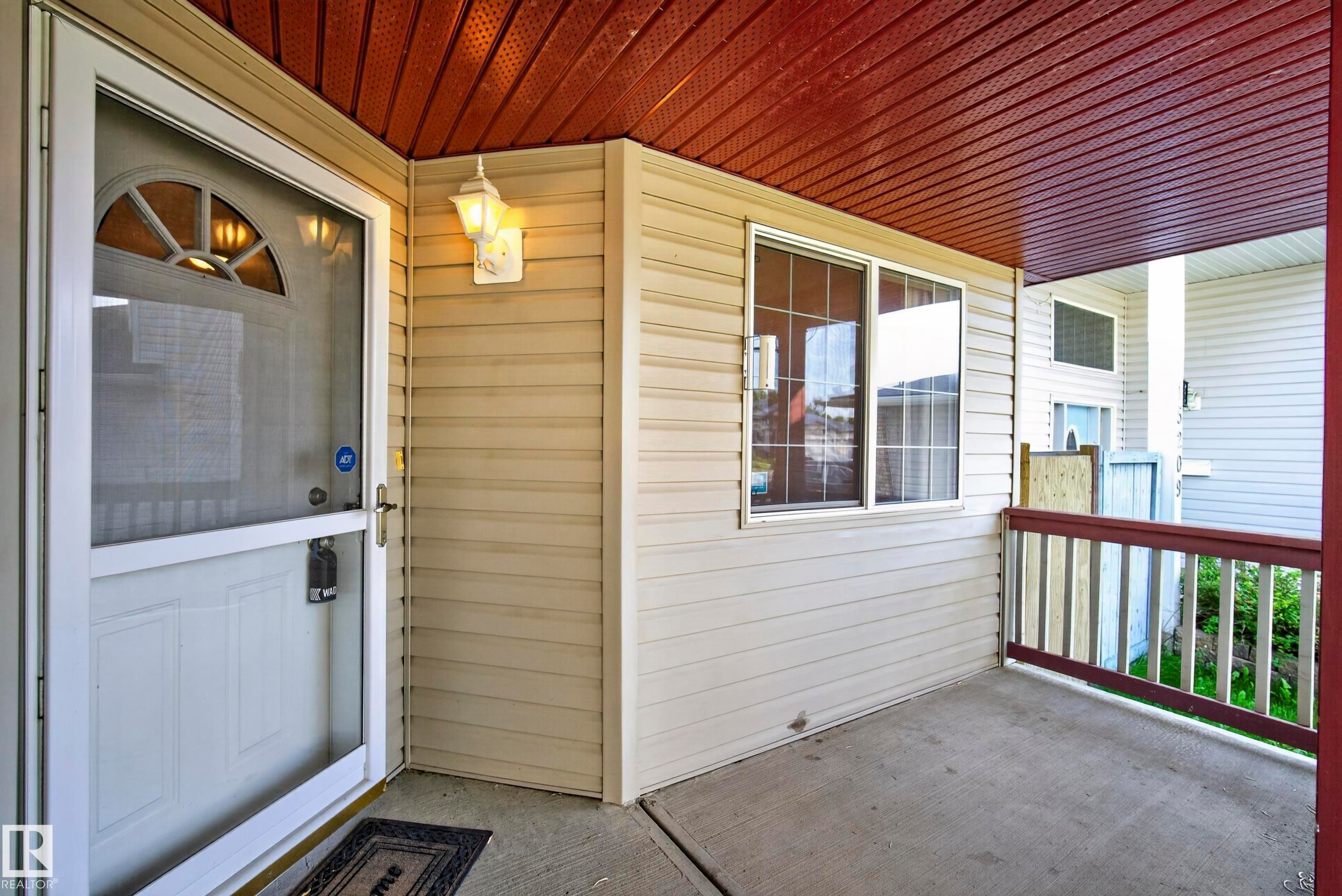 Covered porch featuring durable siding, a decorative entry light, and a window with grid detailing - 15213 49A Street Nw, Edmonton, AB