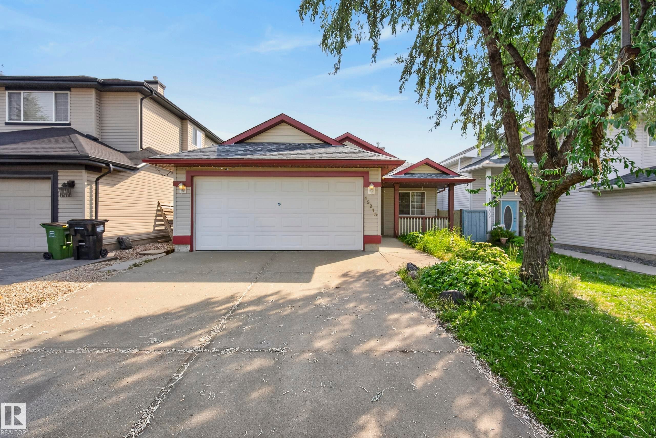 Attached front-entry garage with a concrete driveway, covered porch with wood railing, and shingle roofing - 15213 49A Street Nw, Edmonton, AB