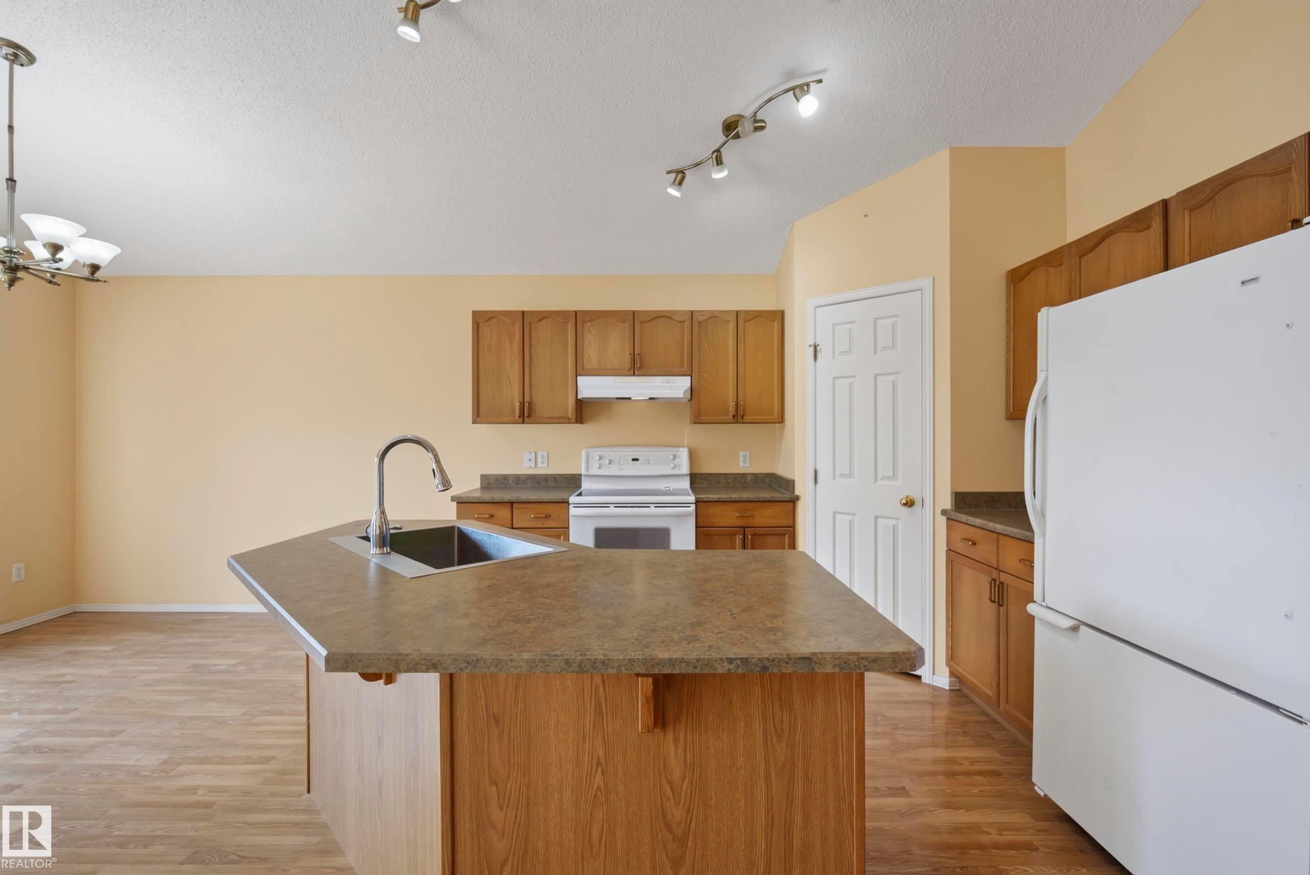 Kitchen featuring wood-finish cabinetry, a central island with an integrated sink, laminate countertops, and hard-surface flooring - 15213 49A Street Nw, Edmonton, AB