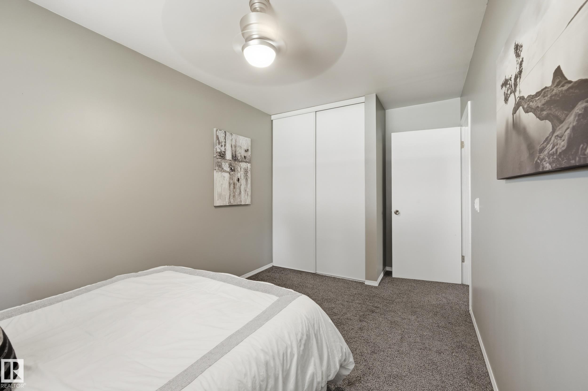 Bright secondary bedroom featuring neutral wall finishes, carpeted flooring, a ceiling-mounted light fixture, and dual closets with white panel doors providing ample storage - 10552 45 Street Nw, Edmonton, AB