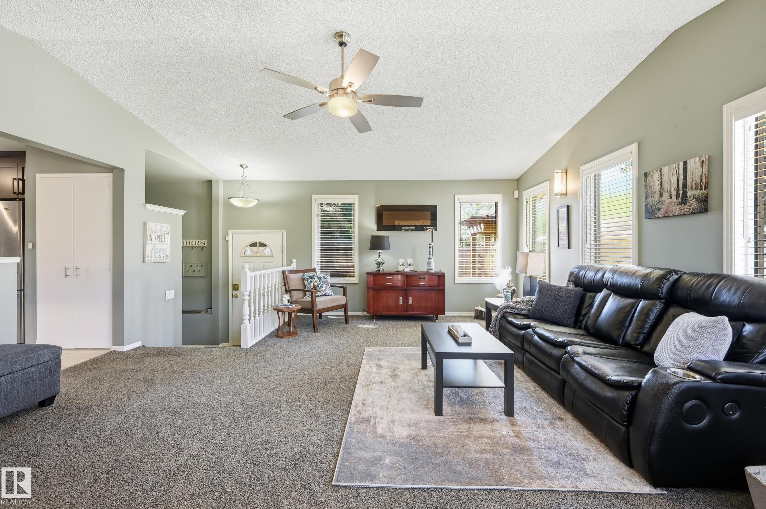 Spacious living area featuring a vaulted ceiling with a ceiling fan, numerous windows with blinds, and built-in wall sconces - 10552 45 Street Nw, Edmonton, AB