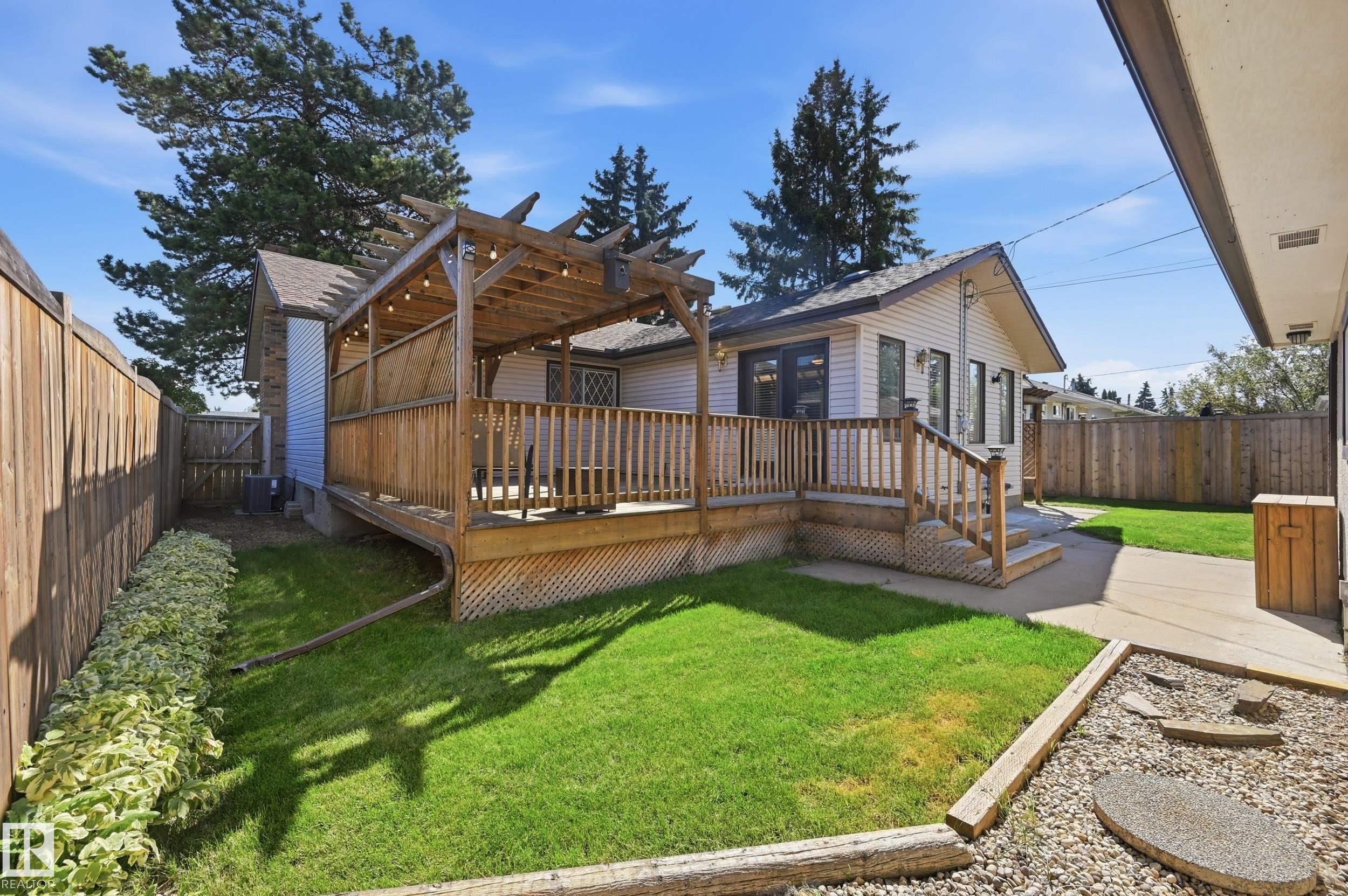 Expansive backyard with a wooden deck, slatted pergola, and manicured lawn - 10552 45 Street Nw, Edmonton, AB