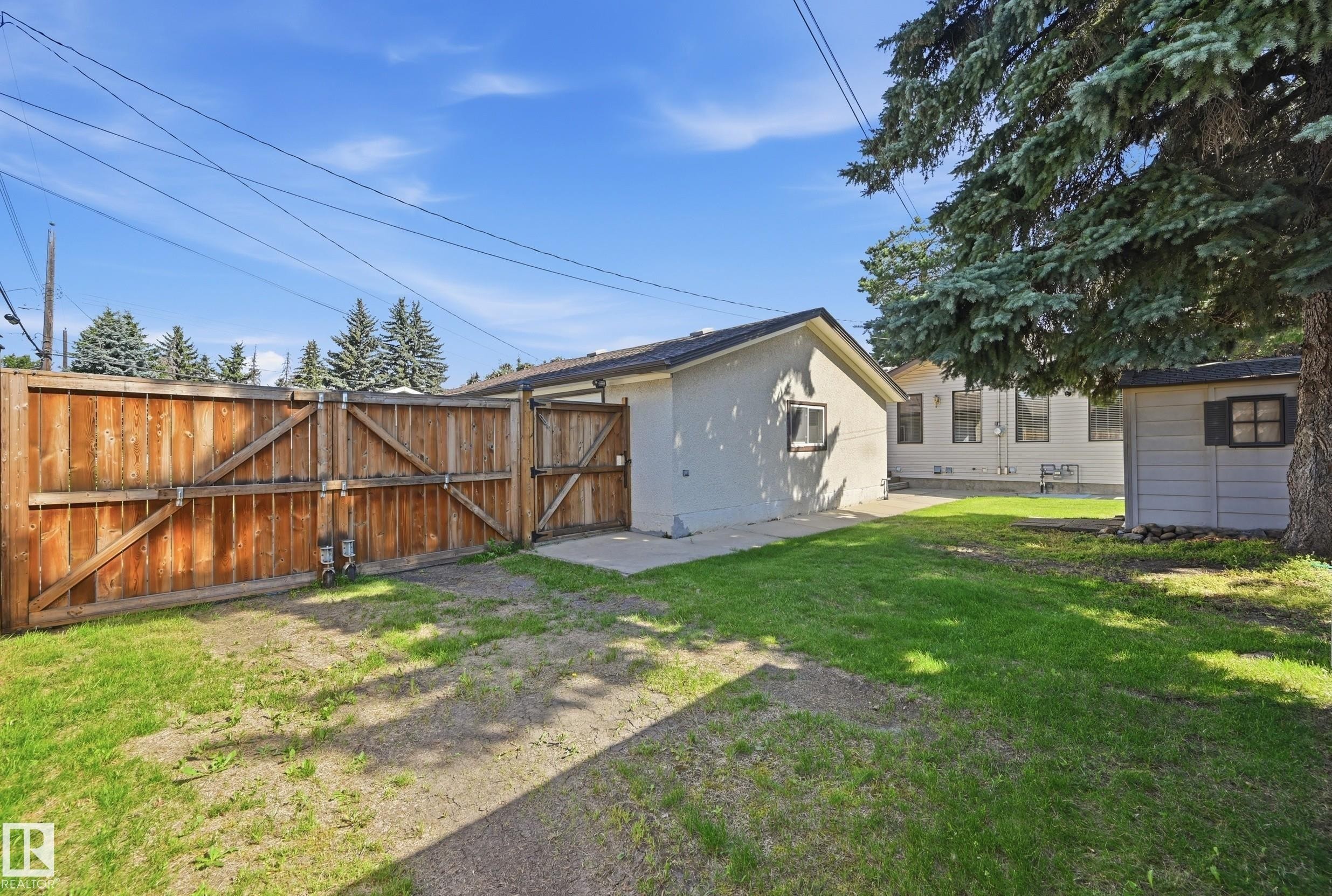Expansive backyard featuring a wood privacy fence, concrete patio, detached shed, and mature trees - 10552 45 Street Nw, Edmonton, AB