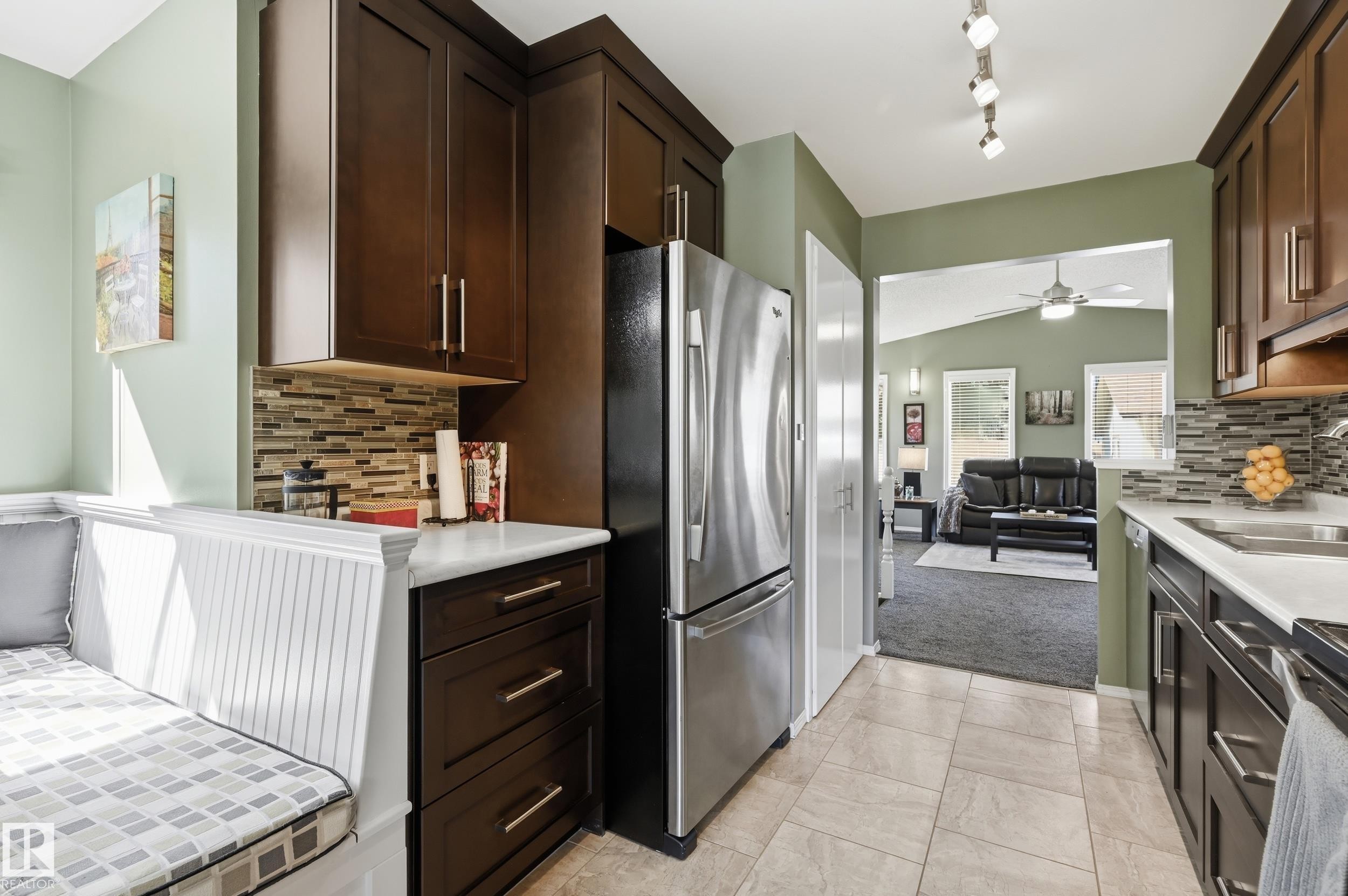 Kitchen featuring dark wood-finish cabinetry, white countertops, mosaic tile backsplash, stainless steel appliances, and built-in bench seating - 10552 45 Street Nw, Edmonton, AB