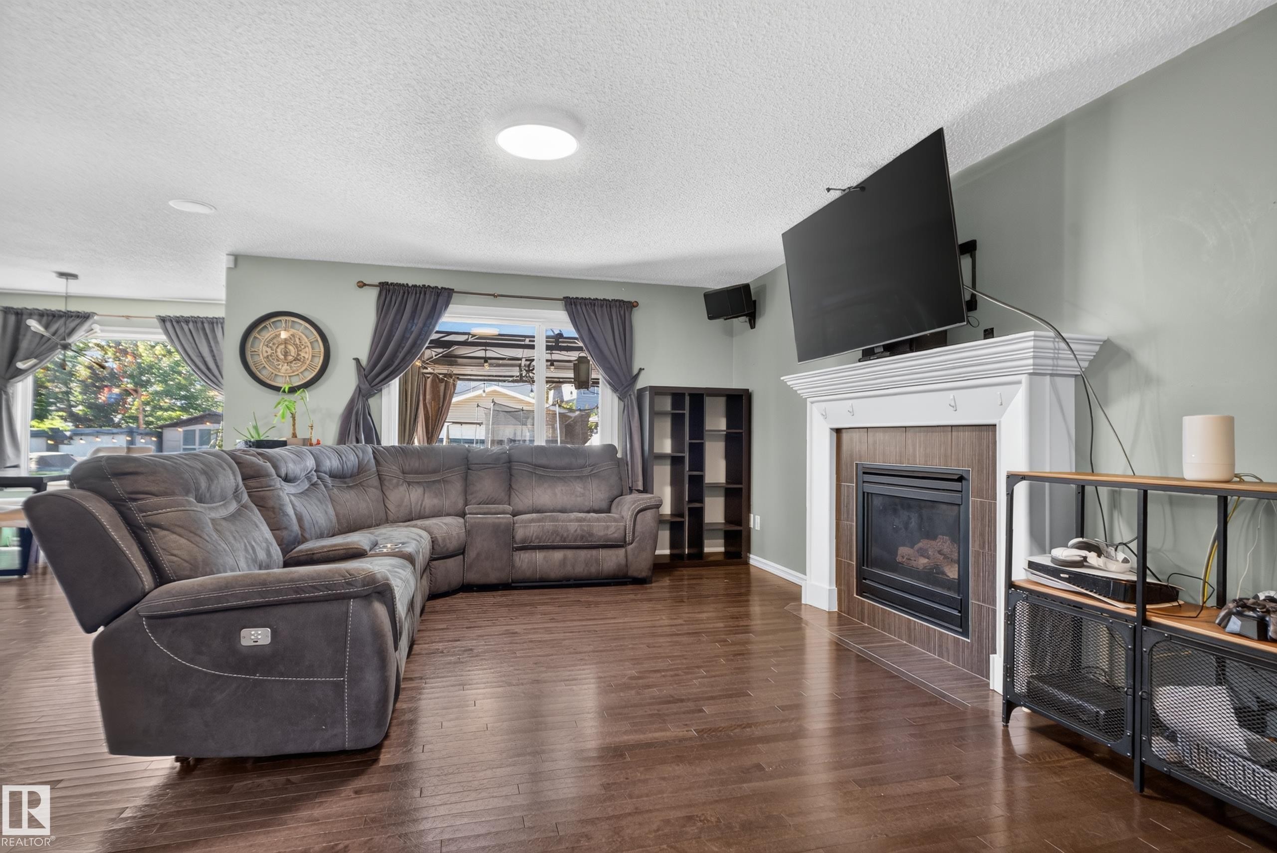 Wood-finish flooring, recessed lighting, and a fireplace with a white mantel and tile surround - 1332 72 Street Sw, Edmonton, AB