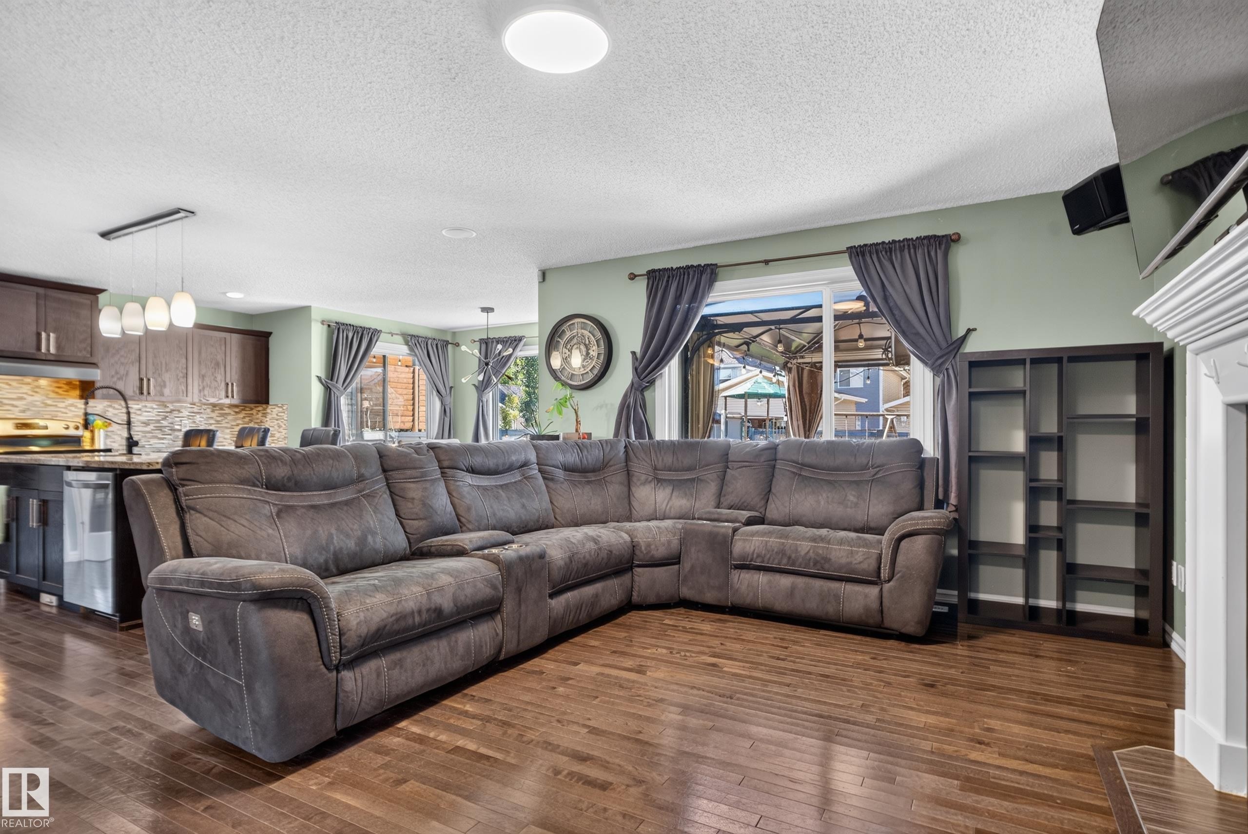 Wood-finish flooring throughout, bright recessed lighting, a modern kitchen with dark cabinetry, and a built-in shelving unit - 1332 72 Street Sw, Edmonton, AB