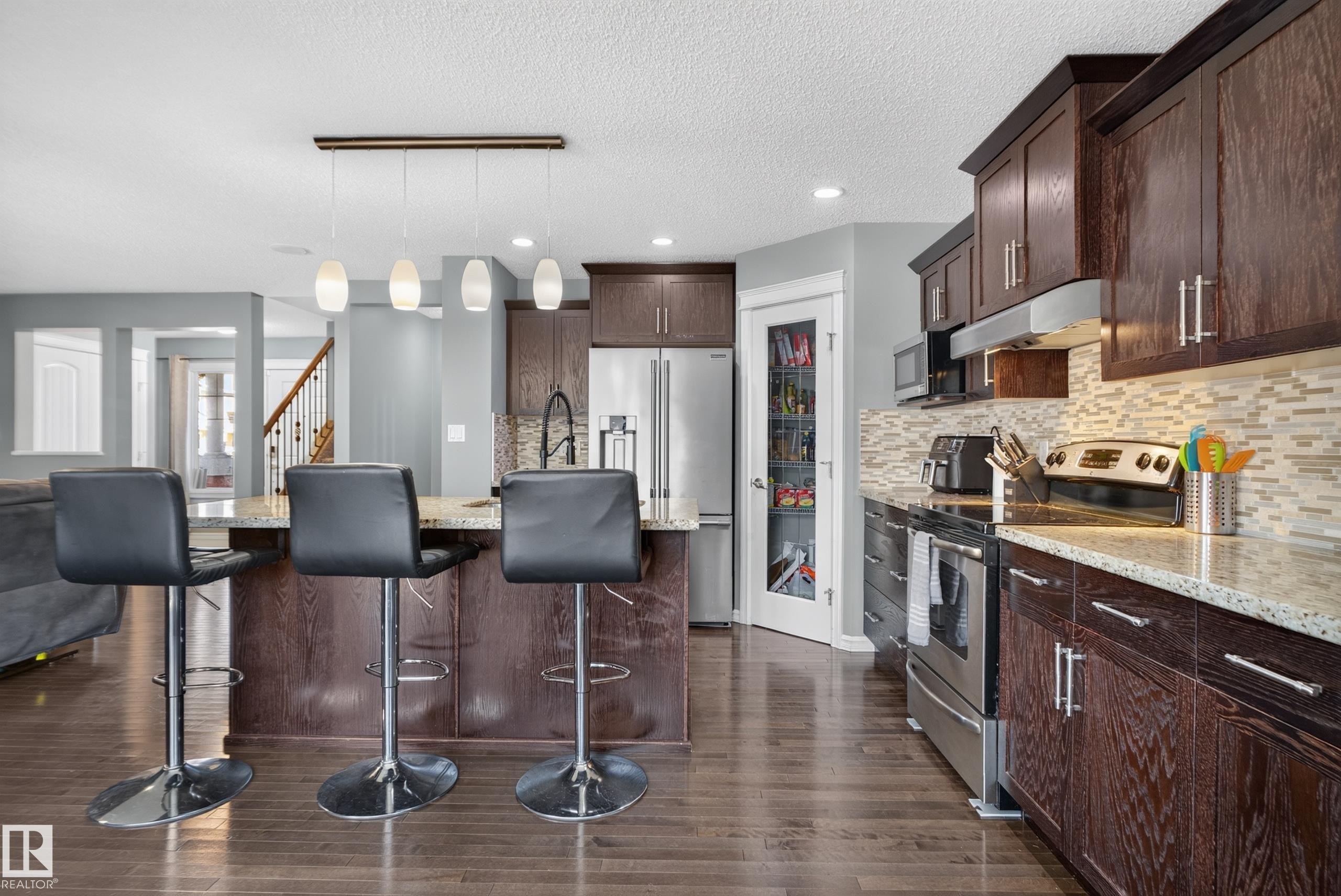 Kitchen with dark wood-finish cabinetry, light-toned countertops, tile backsplash, stainless steel appliances, and a walk-in pantry - 1332 72 Street Sw, Edmonton, AB