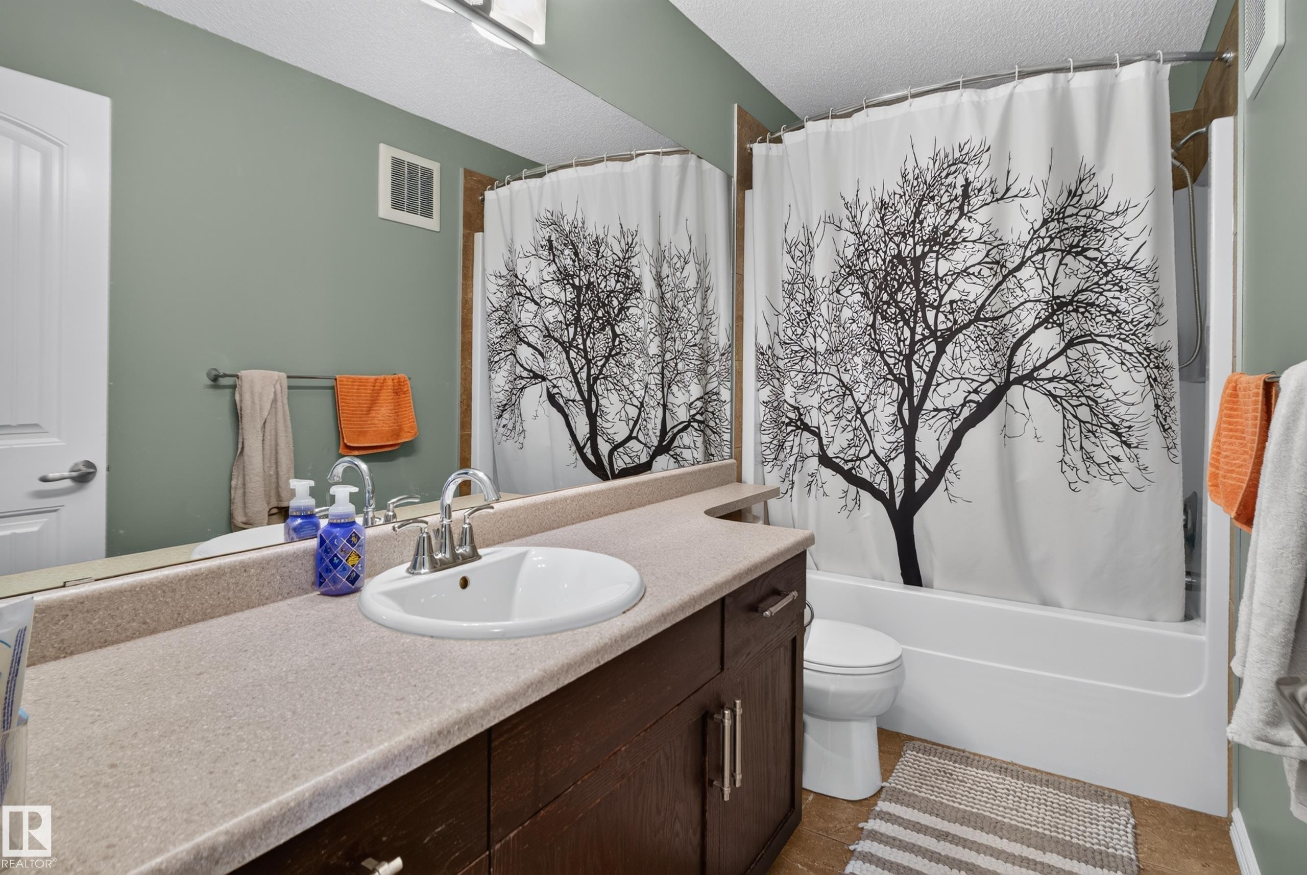 Bathroom featuring a single vanity with an integrated sink, polished chrome faucet, wood-finish cabinetry, and a full-size bathtub - 1332 72 Street Sw, Edmonton, AB