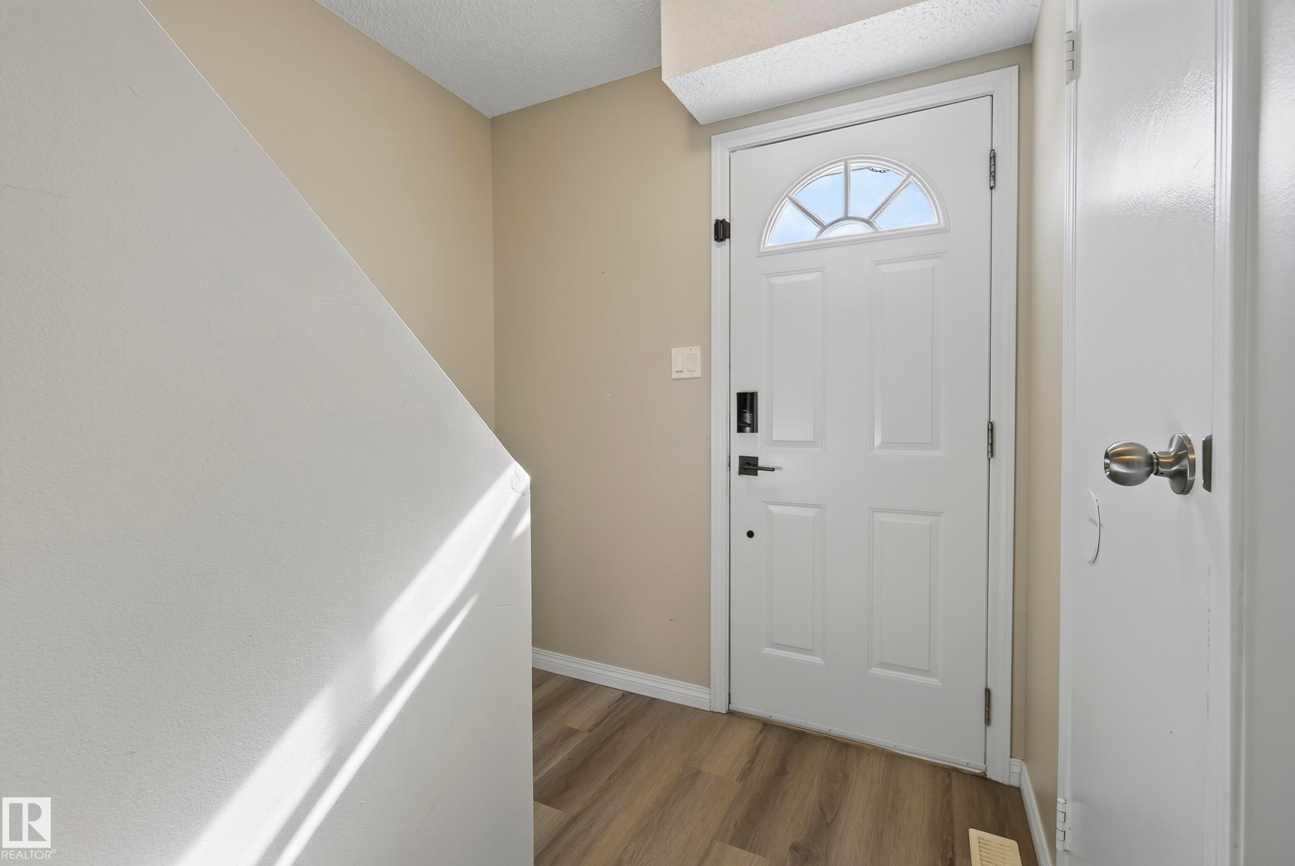 Welcoming foyer with six-panel white entry door featuring a transom window, wood-finish flooring, neutral wall finishes, and white painted railings - 141 Dickinsfield Court Nw, Edmonton, AB