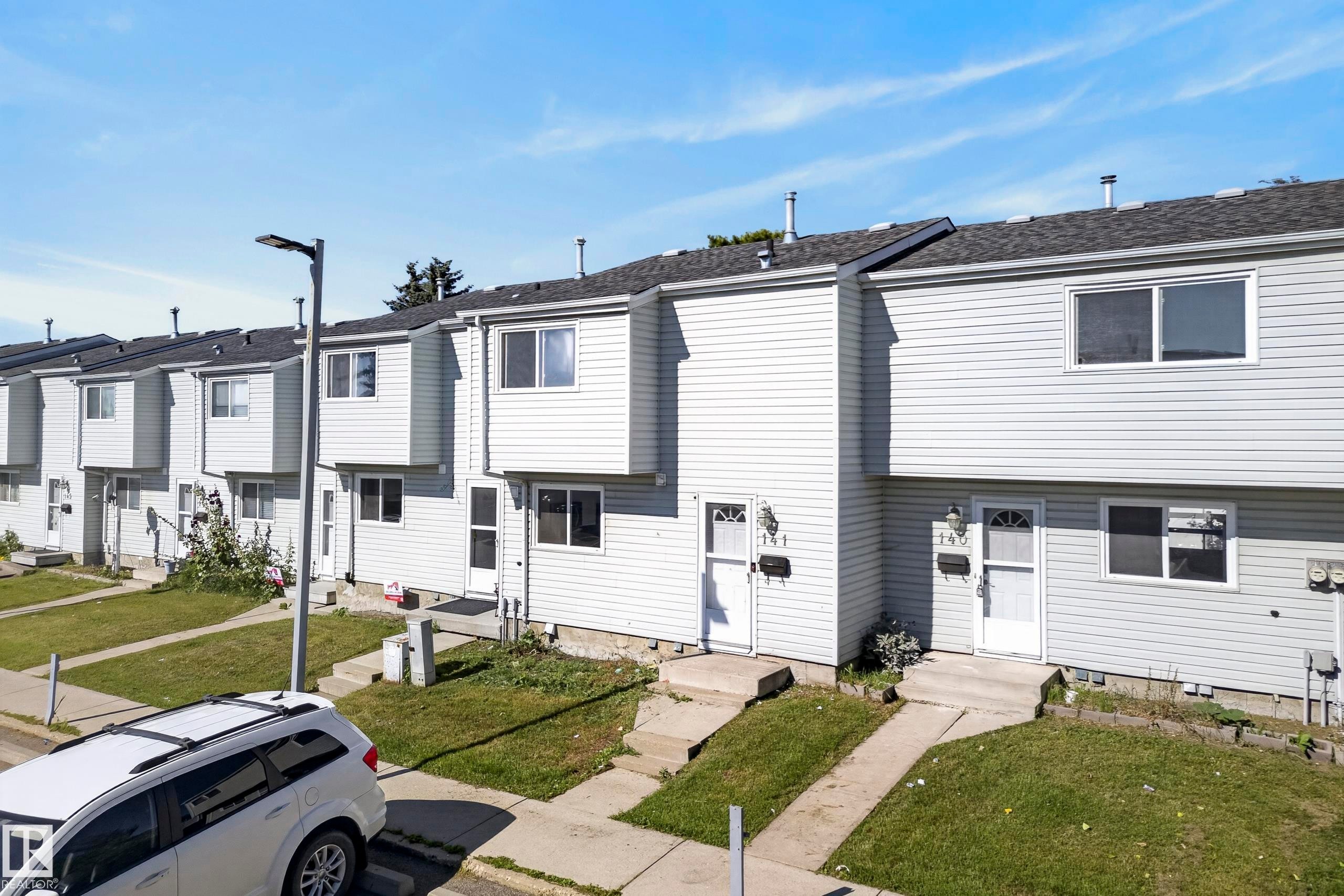 Row of townhomes featuring light-colored siding, individual front entrances, and pitched roofs - 141 Dickinsfield Court Nw, Edmonton, AB