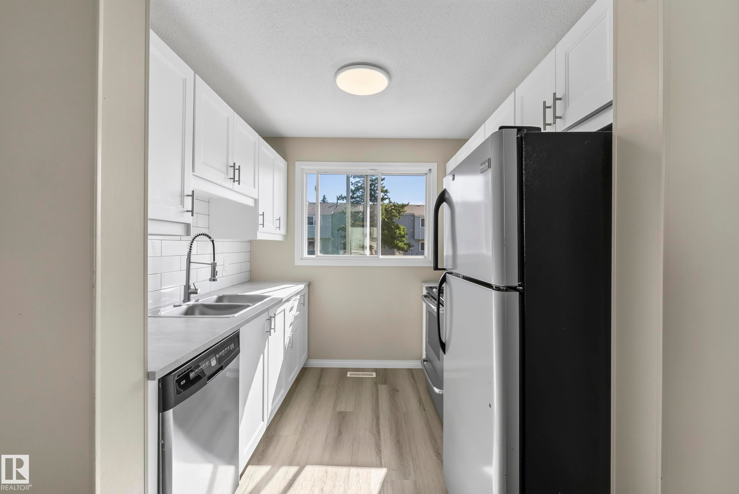 Kitchen with white cabinetry, light-toned countertops, subway tile backsplash, stainless steel appliances, and wood-finish flooring - 141 Dickinsfield Court Nw, Edmonton, AB