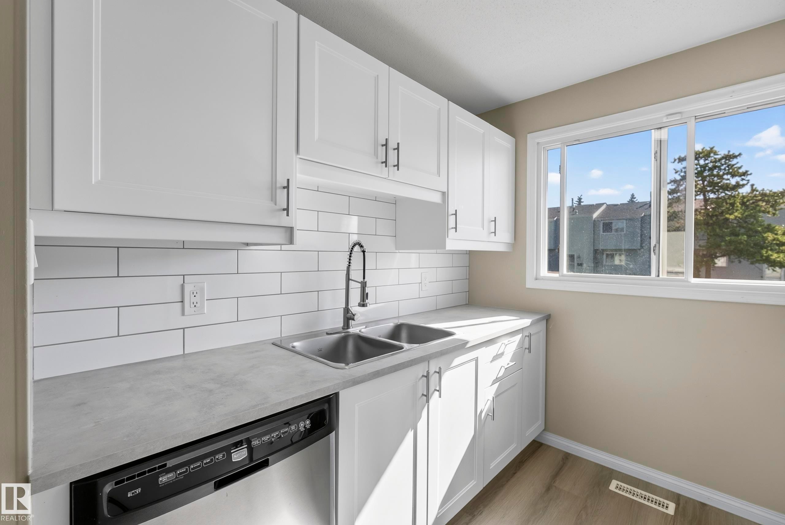 White cabinetry, subway tile backsplash, dual basin stainless steel sink, stainless steel dishwasher, and wood-finish flooring - 141 Dickinsfield Court Nw, Edmonton, AB