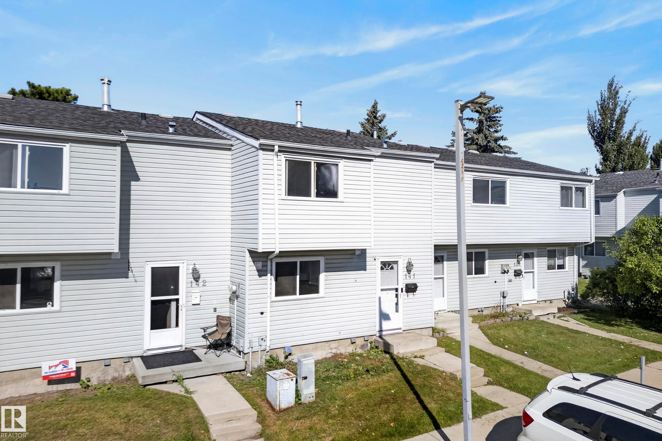 Row of townhomes featuring light-colored siding, dark shingle roofs, and individual front entrances with storm doors - 141 Dickinsfield Court Nw, Edmonton, AB