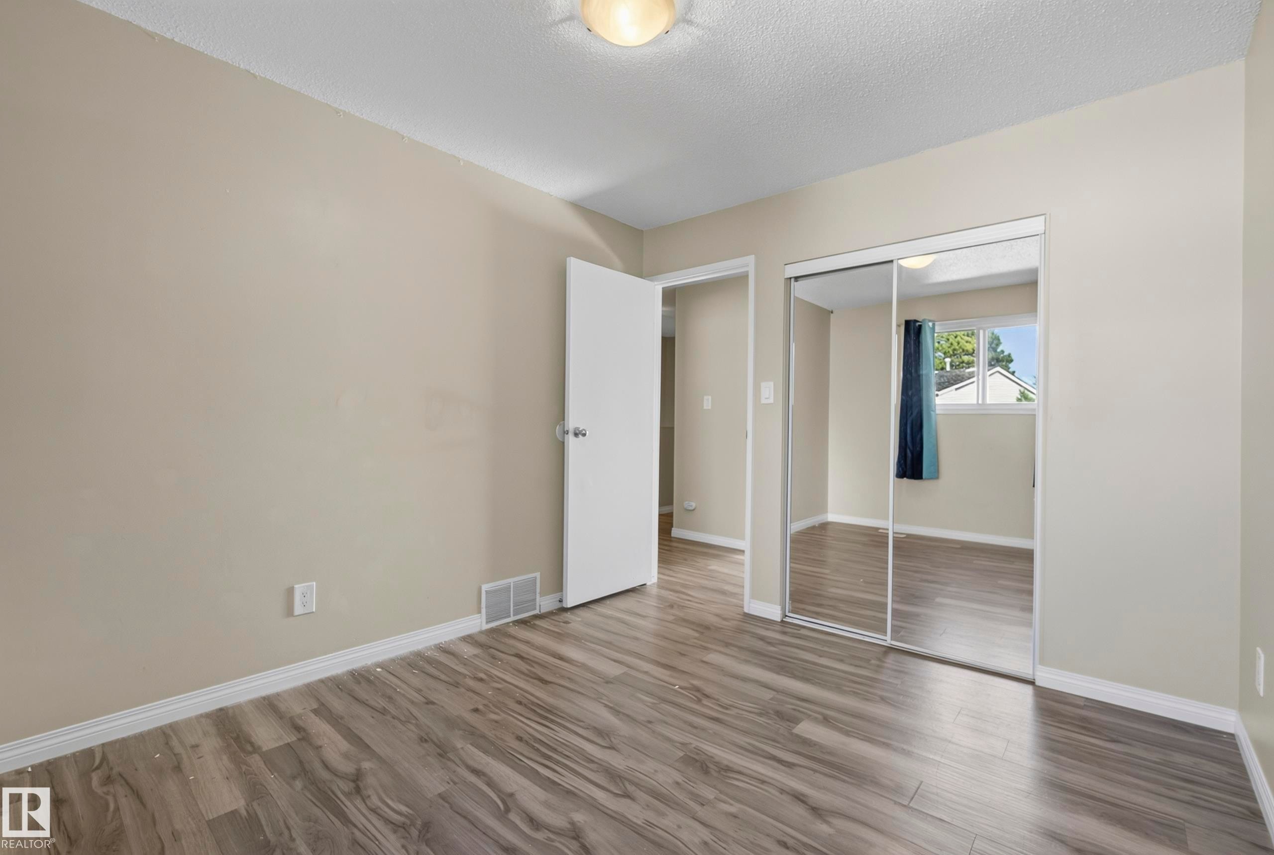Wood-finish flooring, neutral wall tones, and mirrored closet doors - 141 Dickinsfield Court Nw, Edmonton, AB